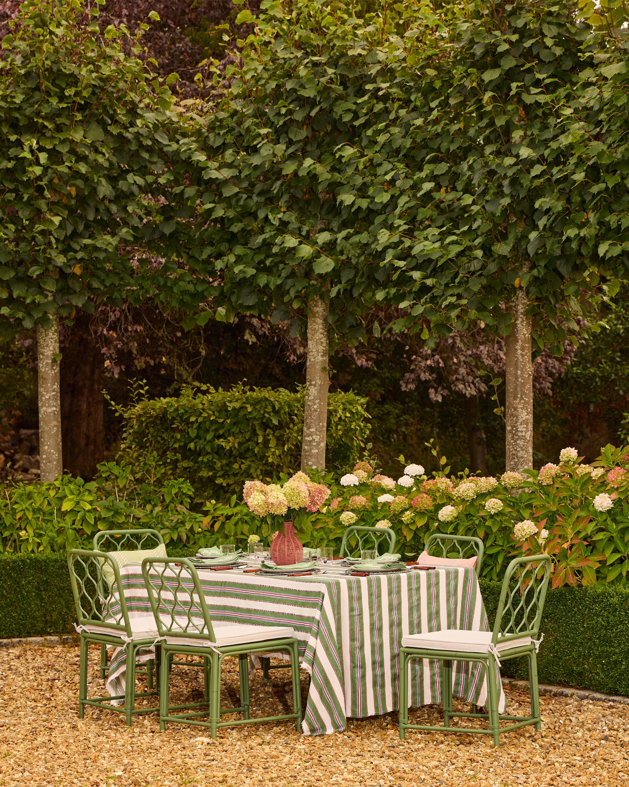 Outdoor dining setup with a striped tablecloth and green chairs in a garden setting.