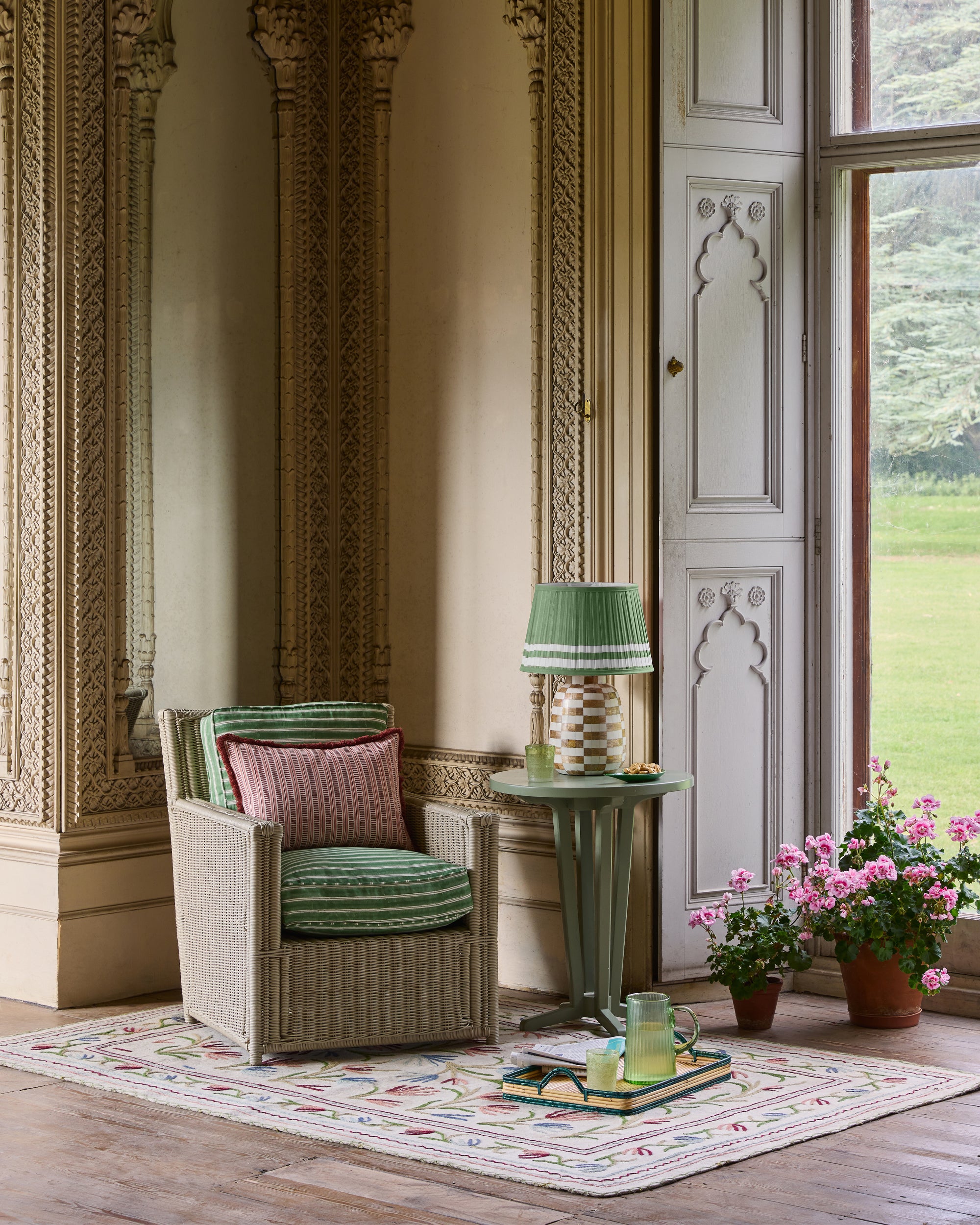 Decorative interior with a wicker chair, small table, and potted plants in a room with ornate walls.