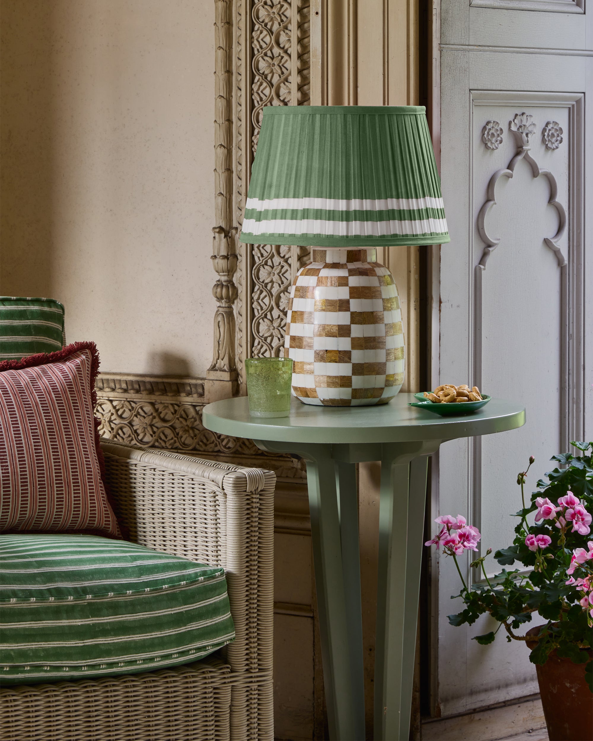 Green lamp on a table with a wicker chair and decorative elements in a room.