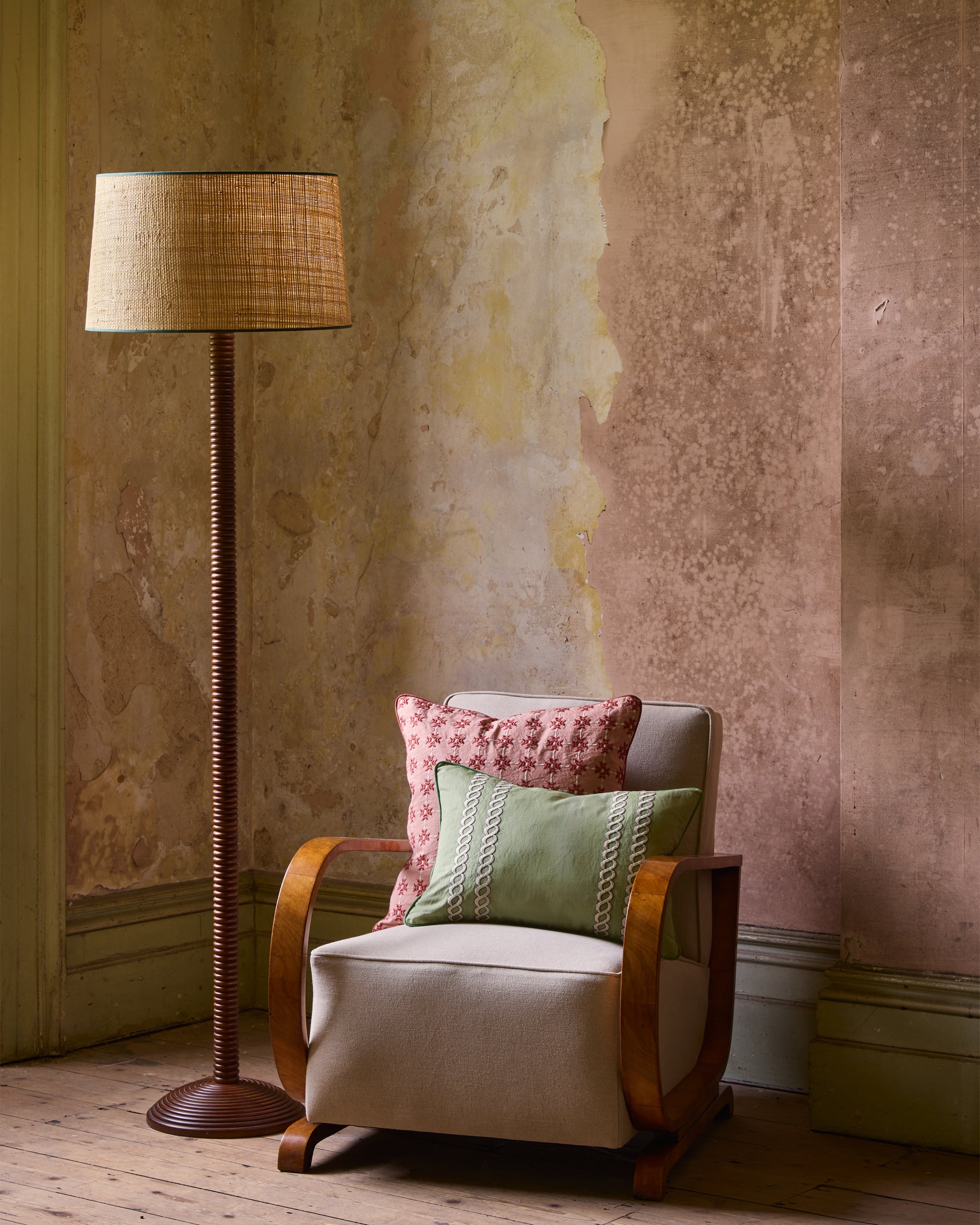 Chair with patterned cushions next to a tall floor lamp against a textured wall.