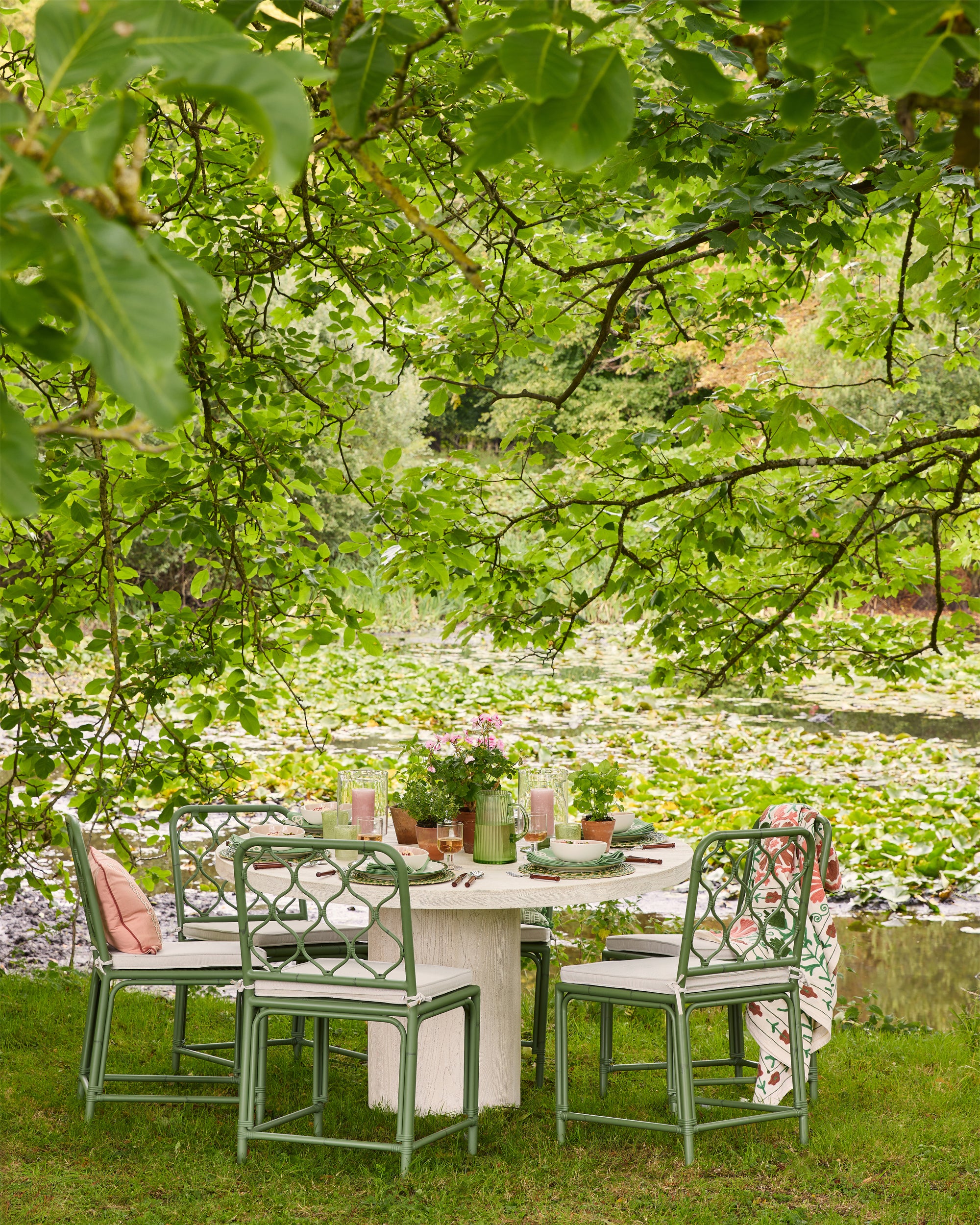 Outdoor dining setup with table and chairs near a pond with lily pads