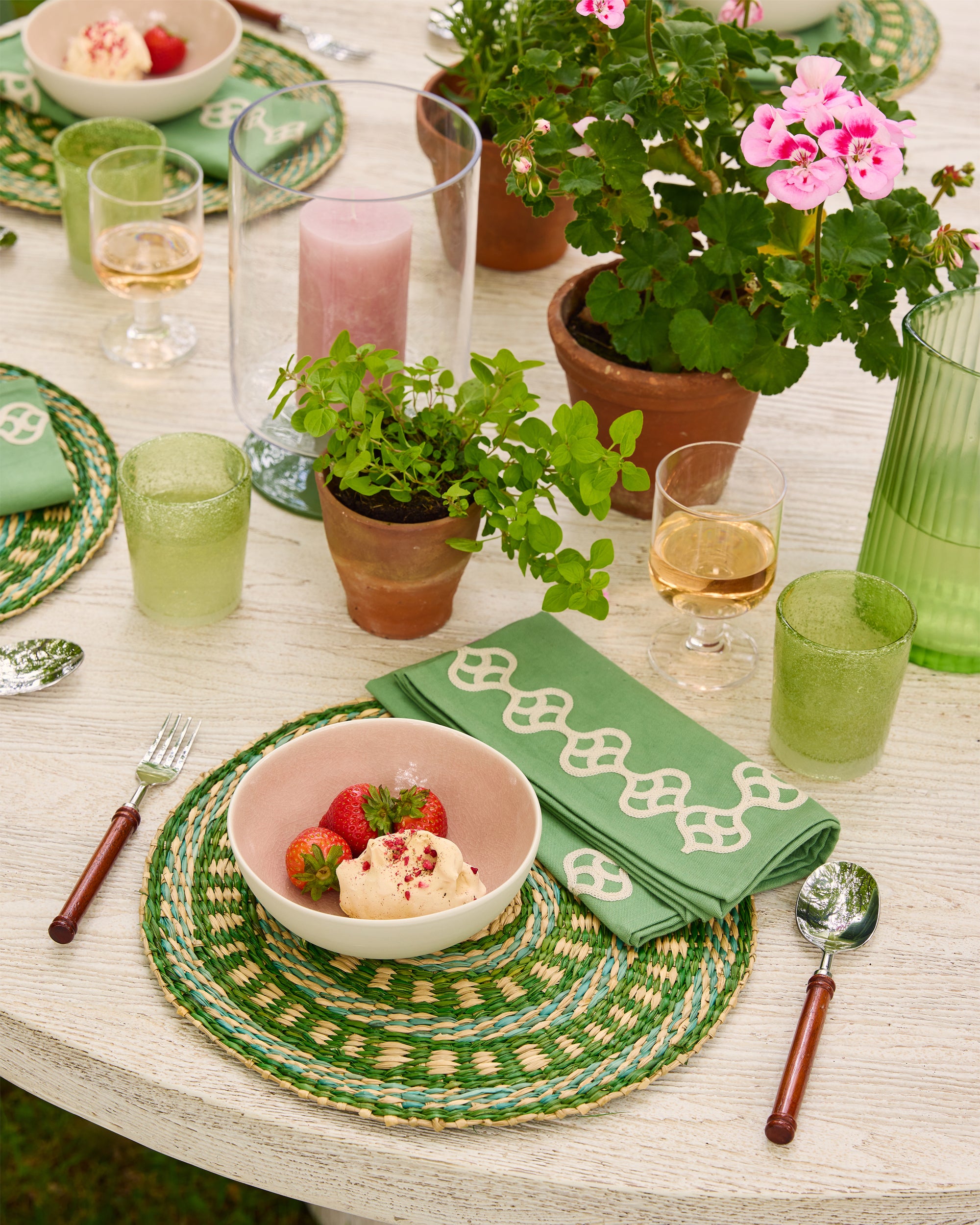 Dining table set with green placemats, glasses, and a bowl of fruit.