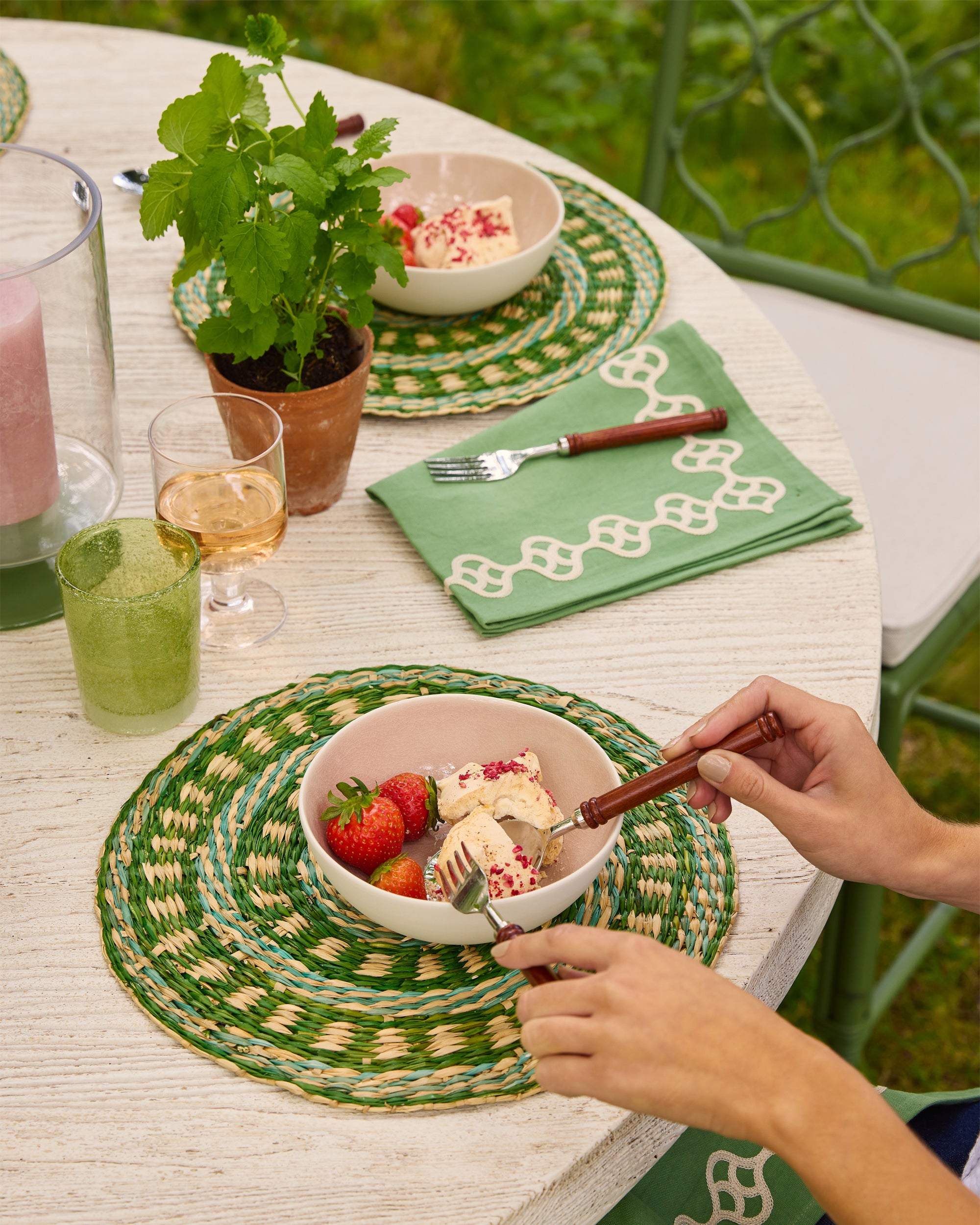 Outdoor dining scene with a table set with green placemats, glasses, and a bowl of ice cream.