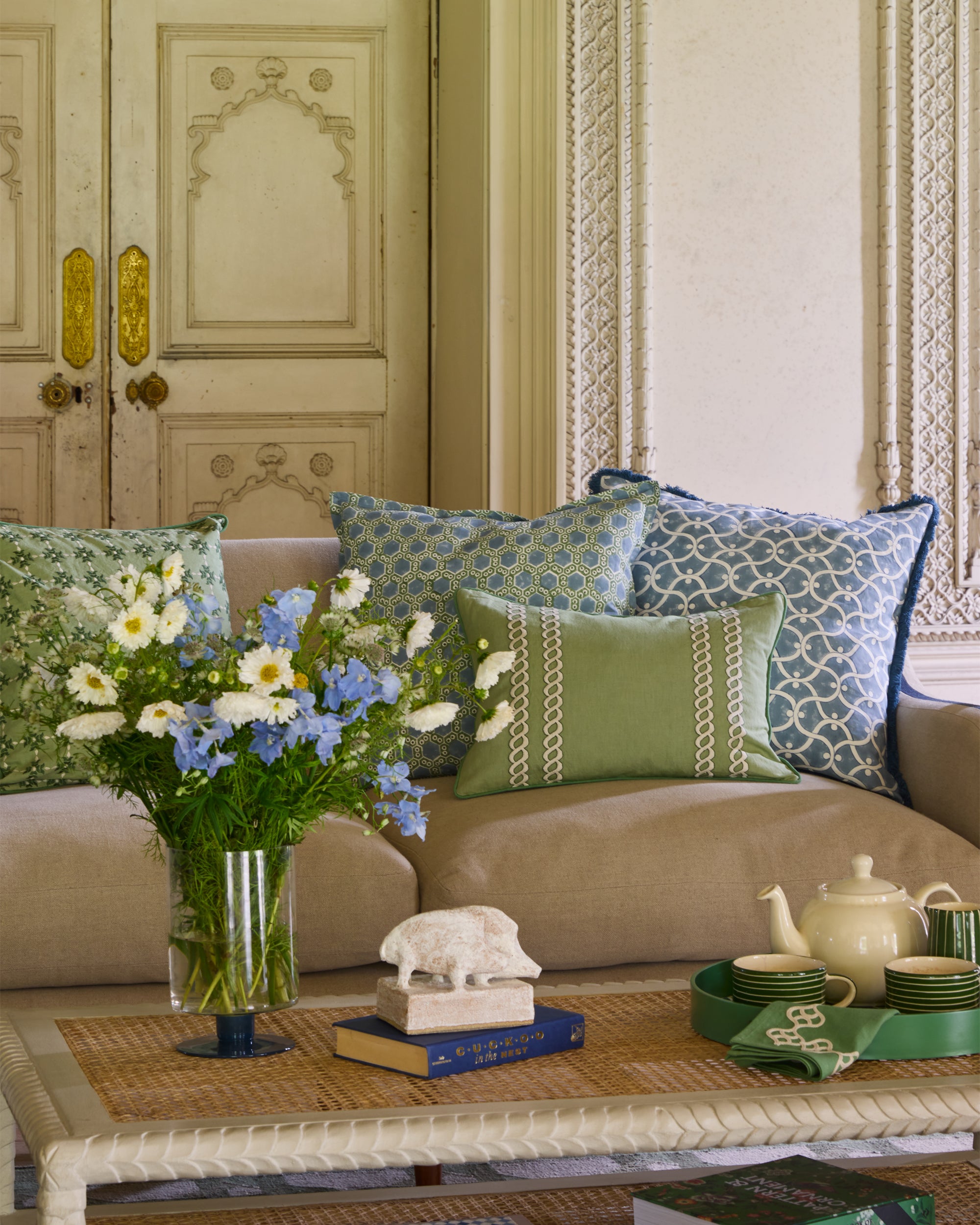 Living room with patterned cushions, flowers, and a teapot on a table.