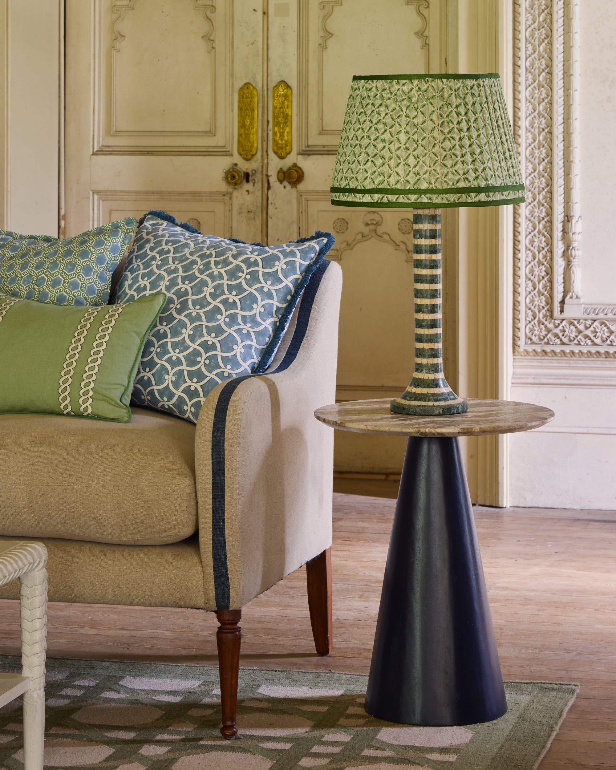 Decorative lamp on a side table next to a sofa with patterned cushions in a room with ornate walls.