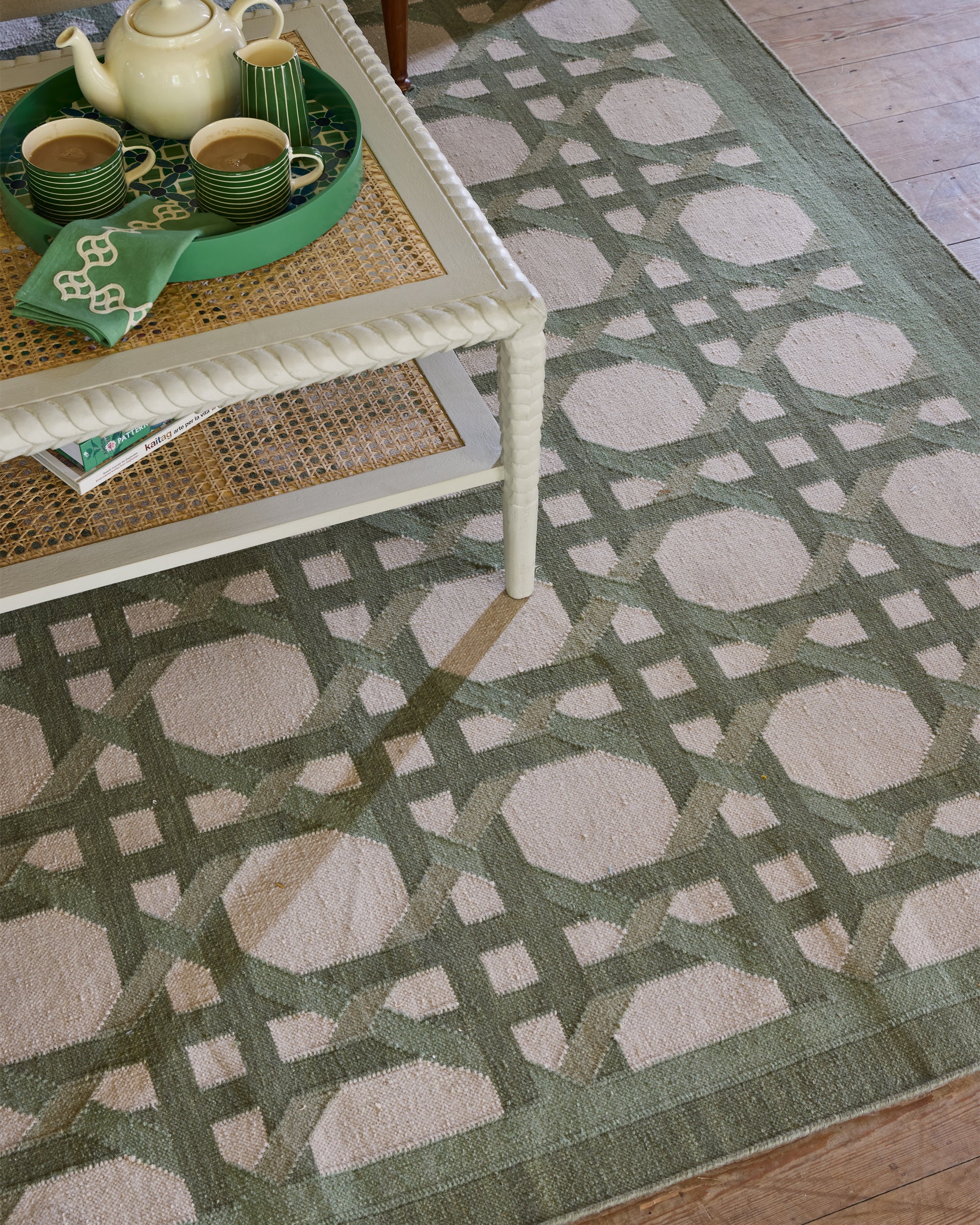 Patterned green and beige rug with a white coffee table and green tray with tea set.