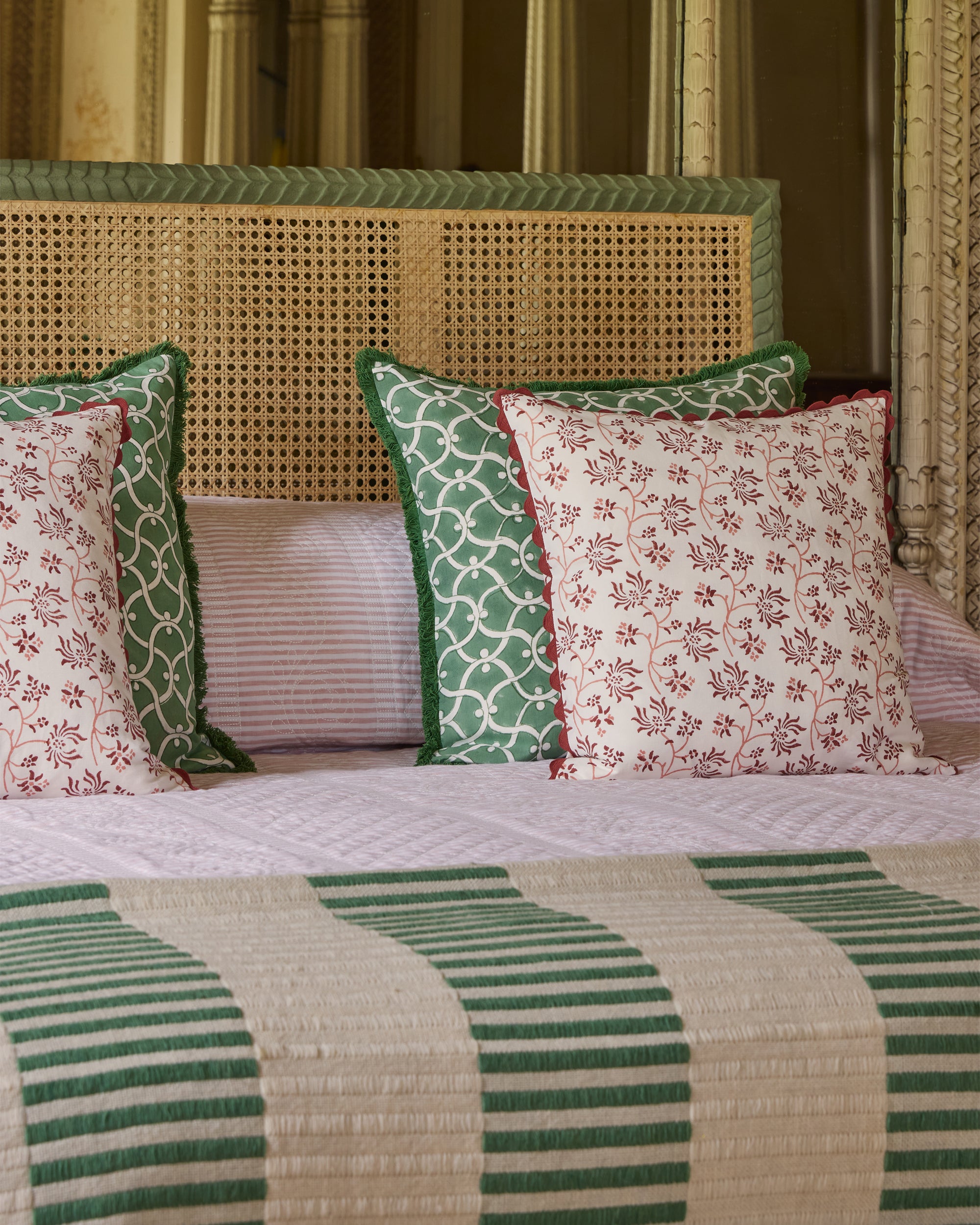 Decorative pillows with green and red patterns on a bed with striped bedding.