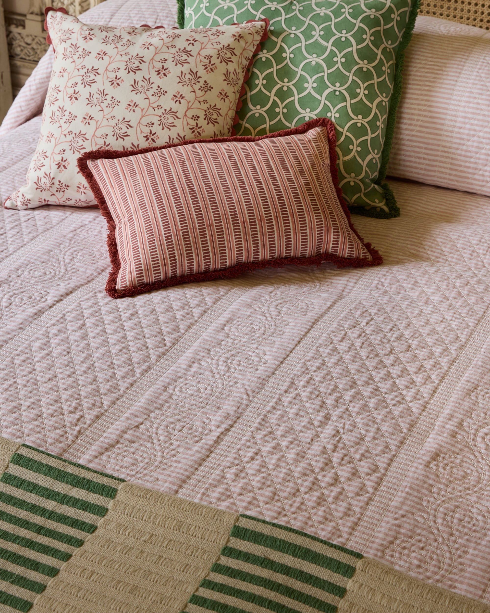 Patterned pillows on a textured bedspread with green and beige tones.