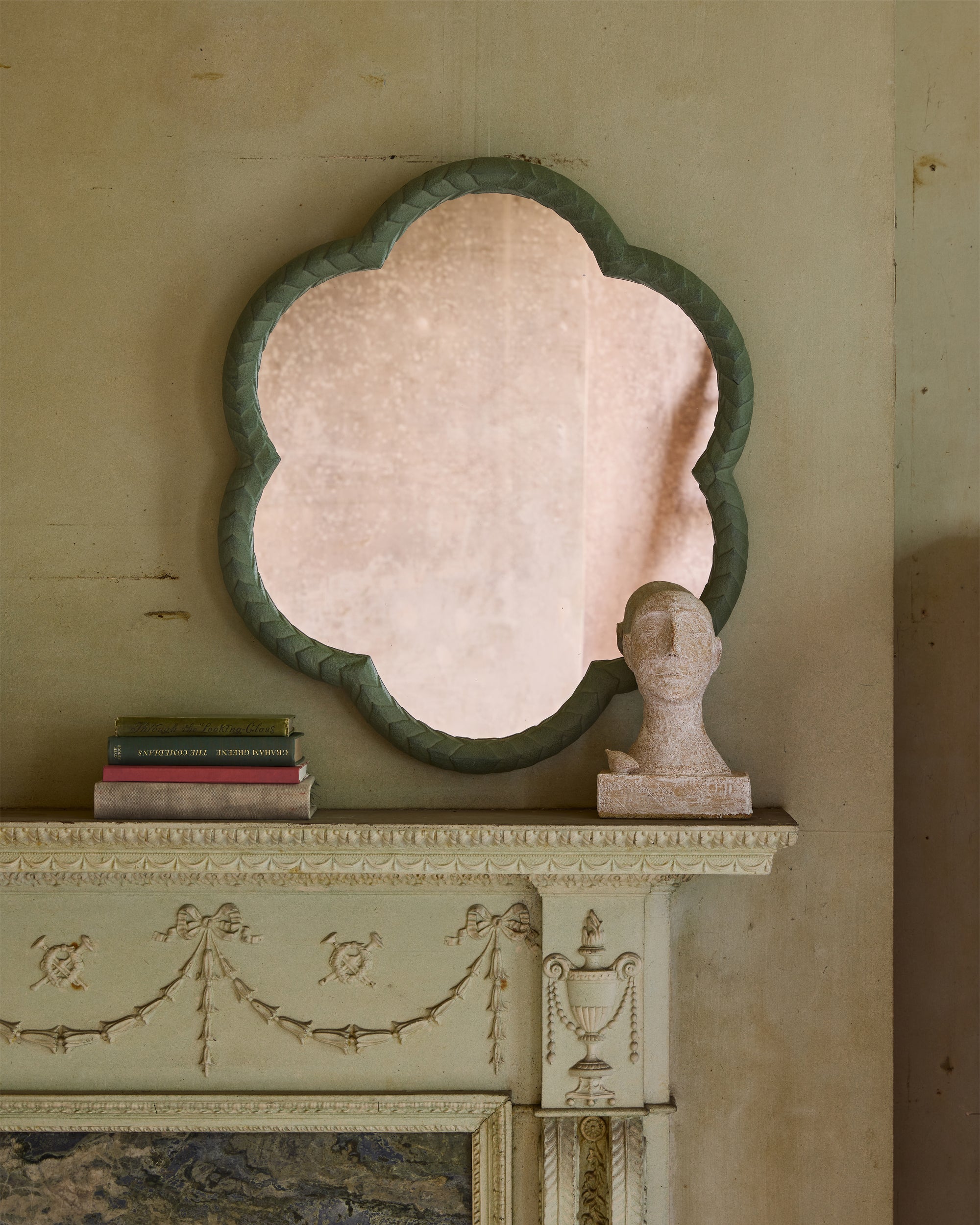 Decorative mirror with a green frame on a wall above a fireplace mantel.