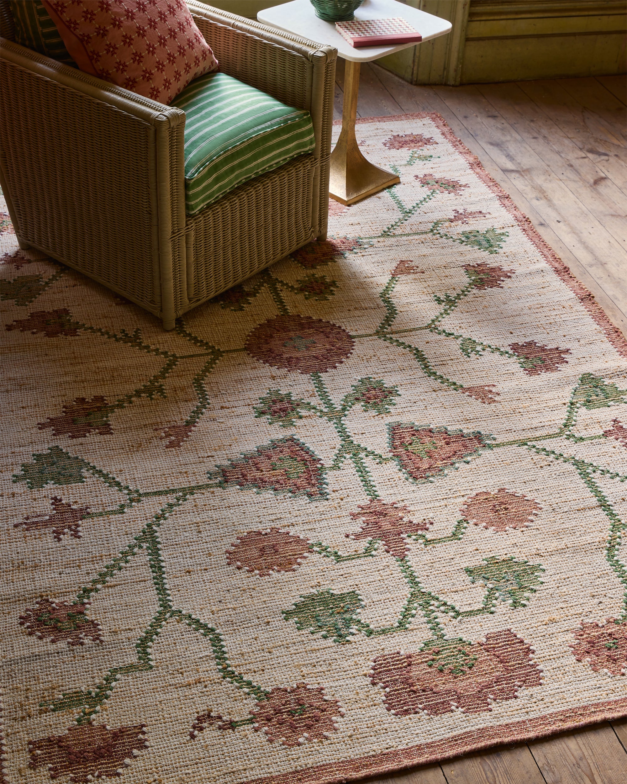 Decorative rug with floral pattern on wooden floor, chair with cushions in the background
