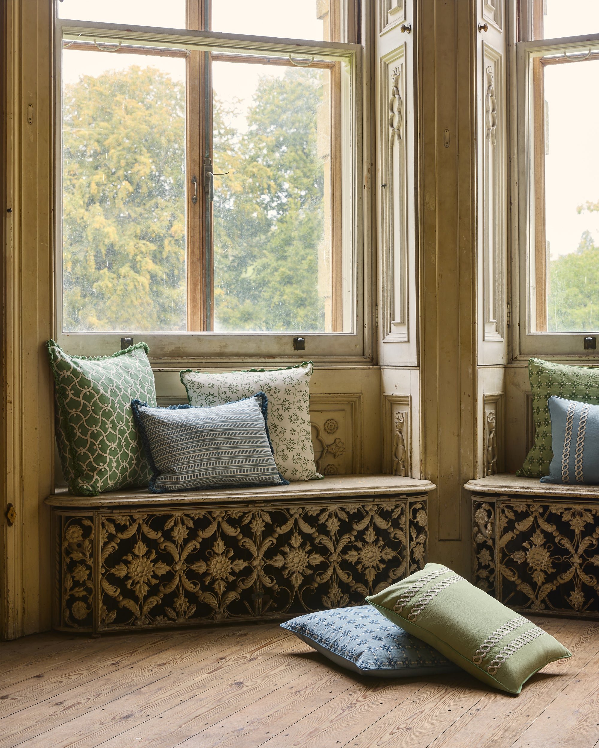 Decorative window seat with patterned cushions in a room with large windows.