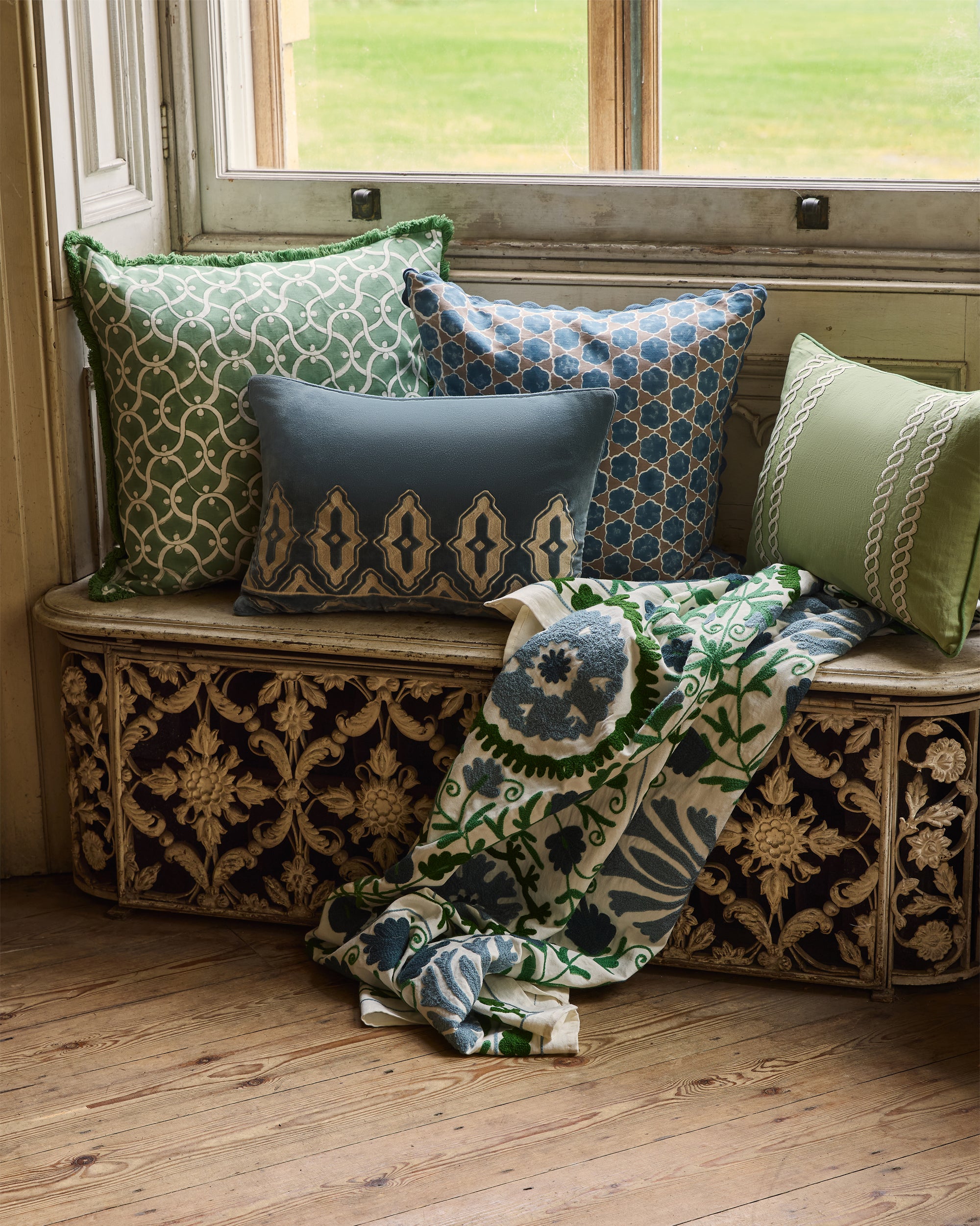 Decorative pillows and blanket on a patterned bench by a window