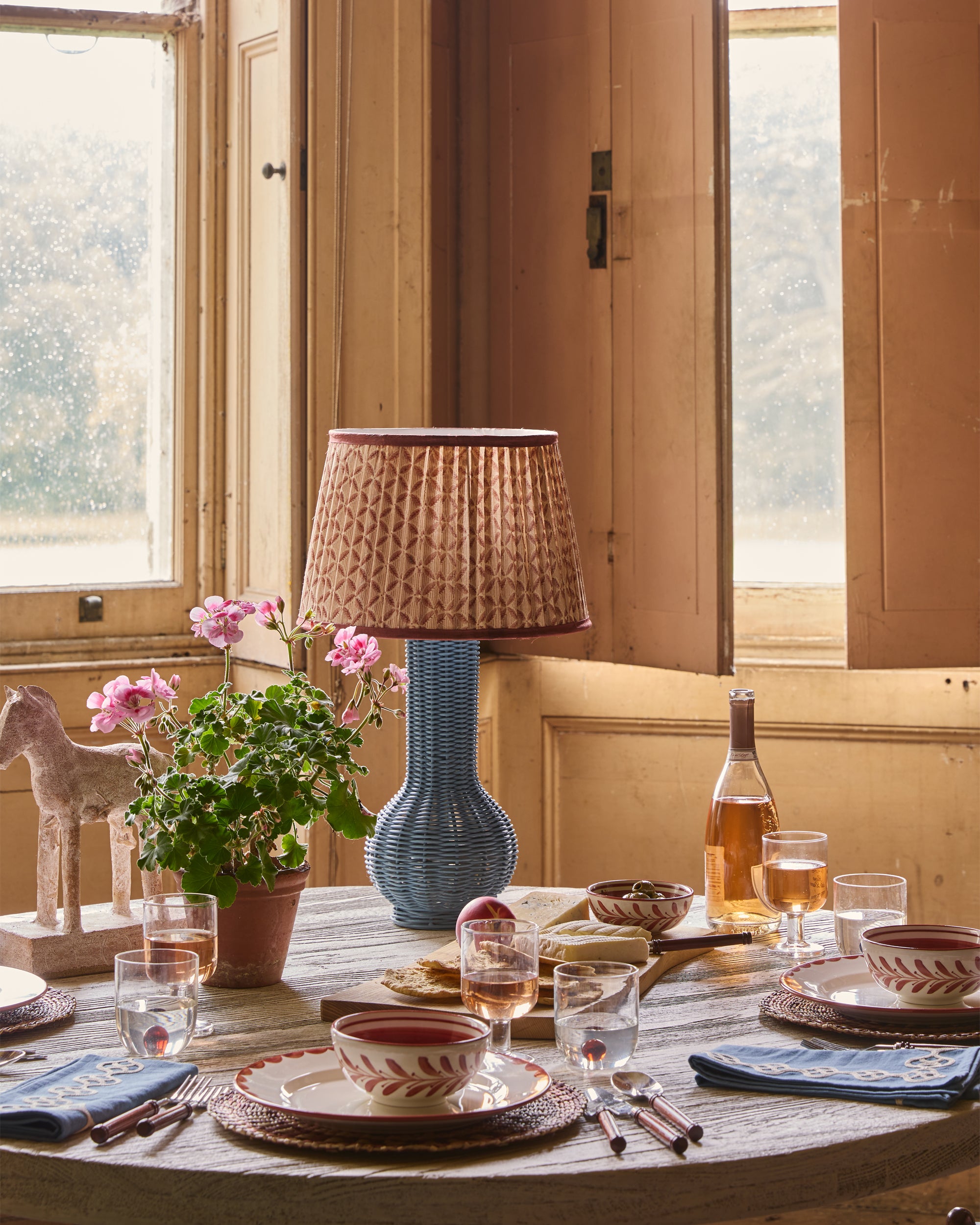 Dining table setting with a lamp, flowers, and wine glasses in a warm-toned room.