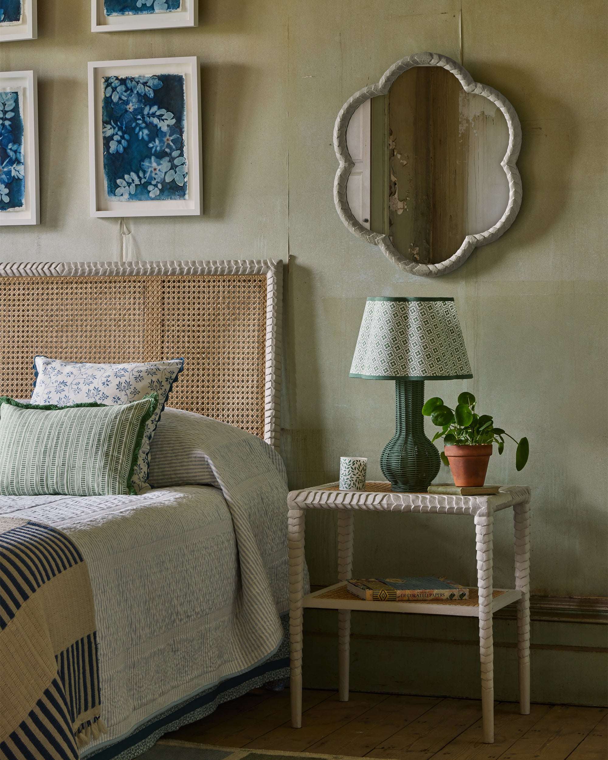 Bedroom with wicker headboard, bedside table with lamp and plant, and decorative mirror.