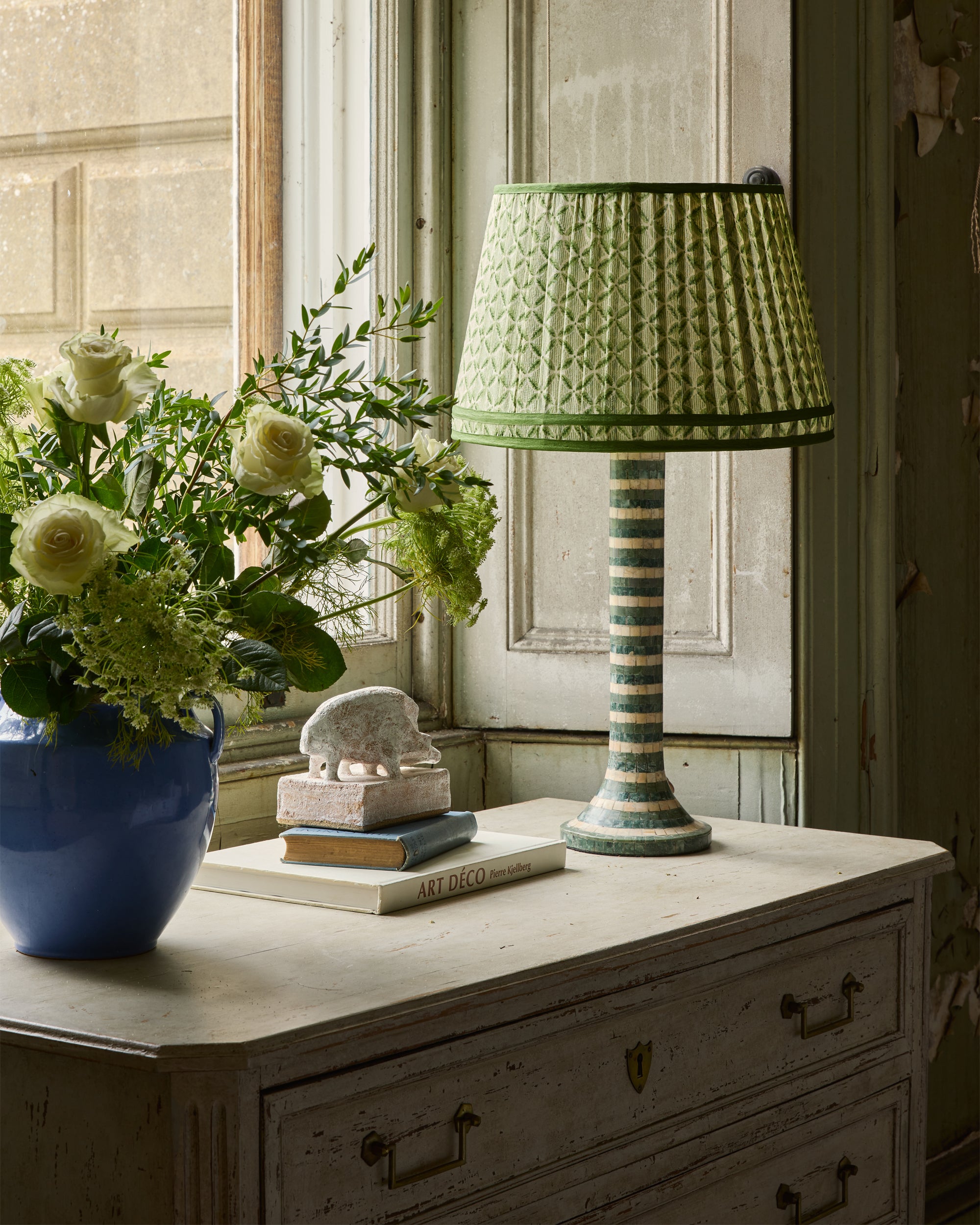 Green striped lamp on a wooden dresser with flowers and books