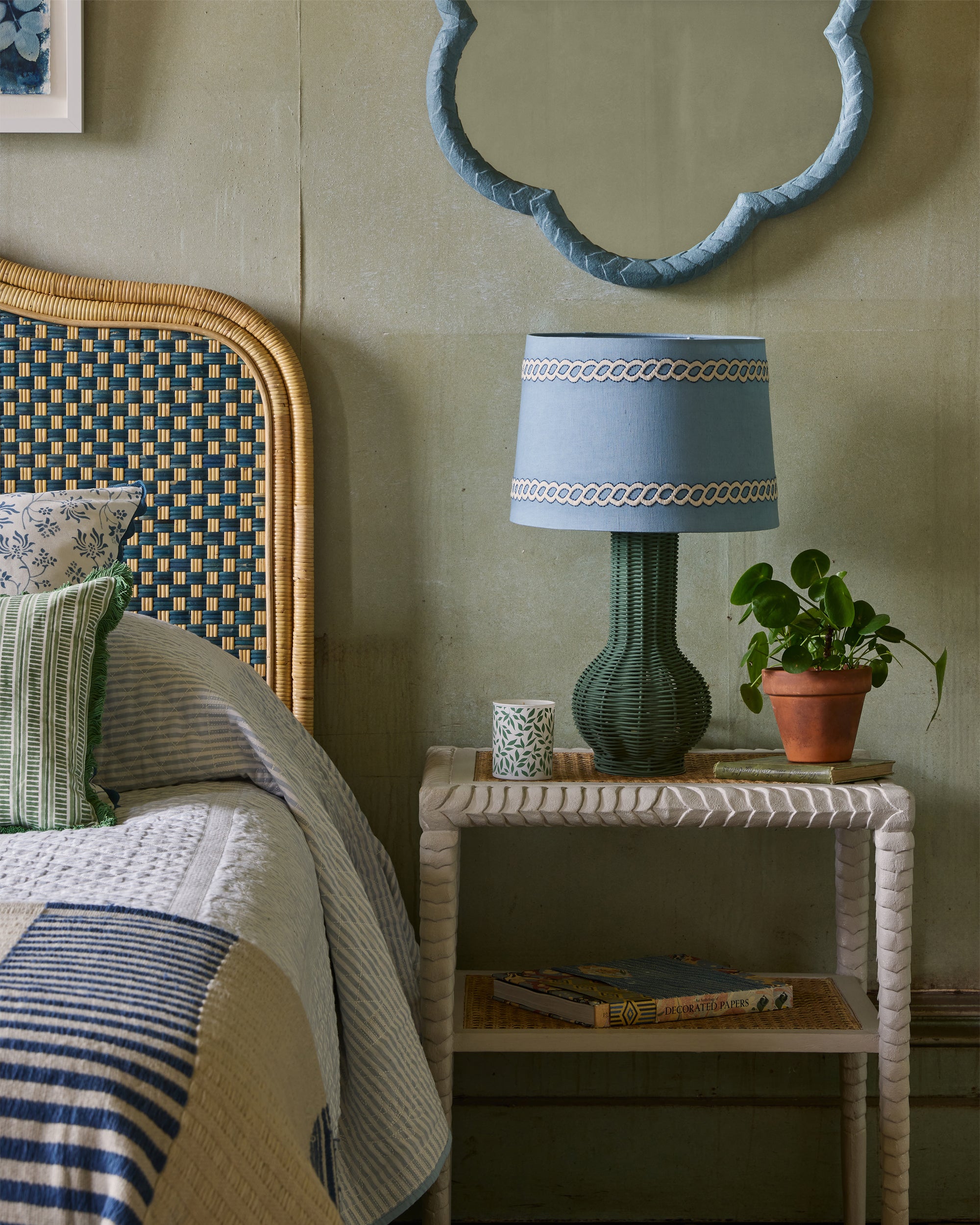 Bedroom with a bed, nightstand, lamp, and plant against a green wall.