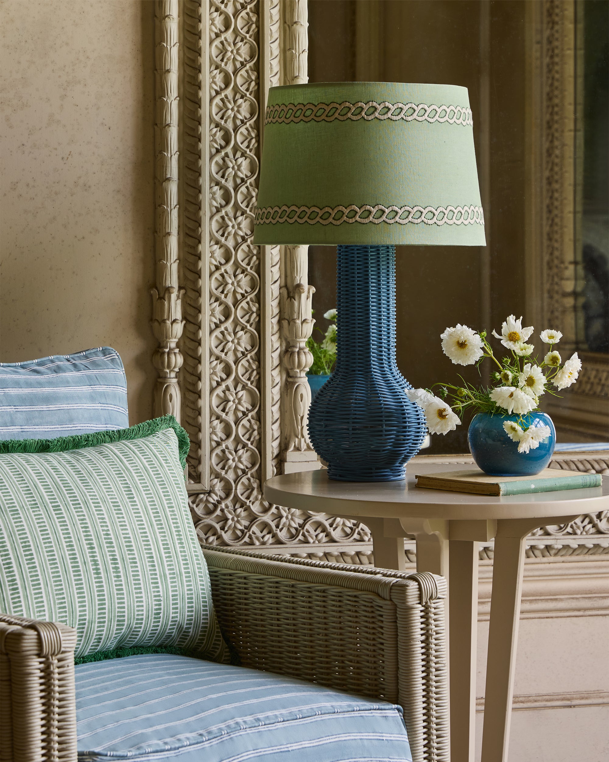 Decorative lamp with green shade on a table next to a wicker chair with striped cushions.