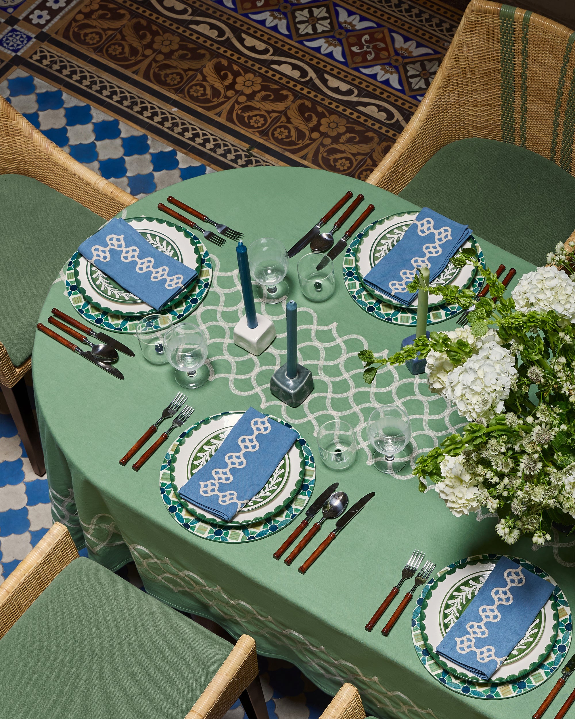 Decorative table setting with green tablecloth and blue place mats on a patterned floor.