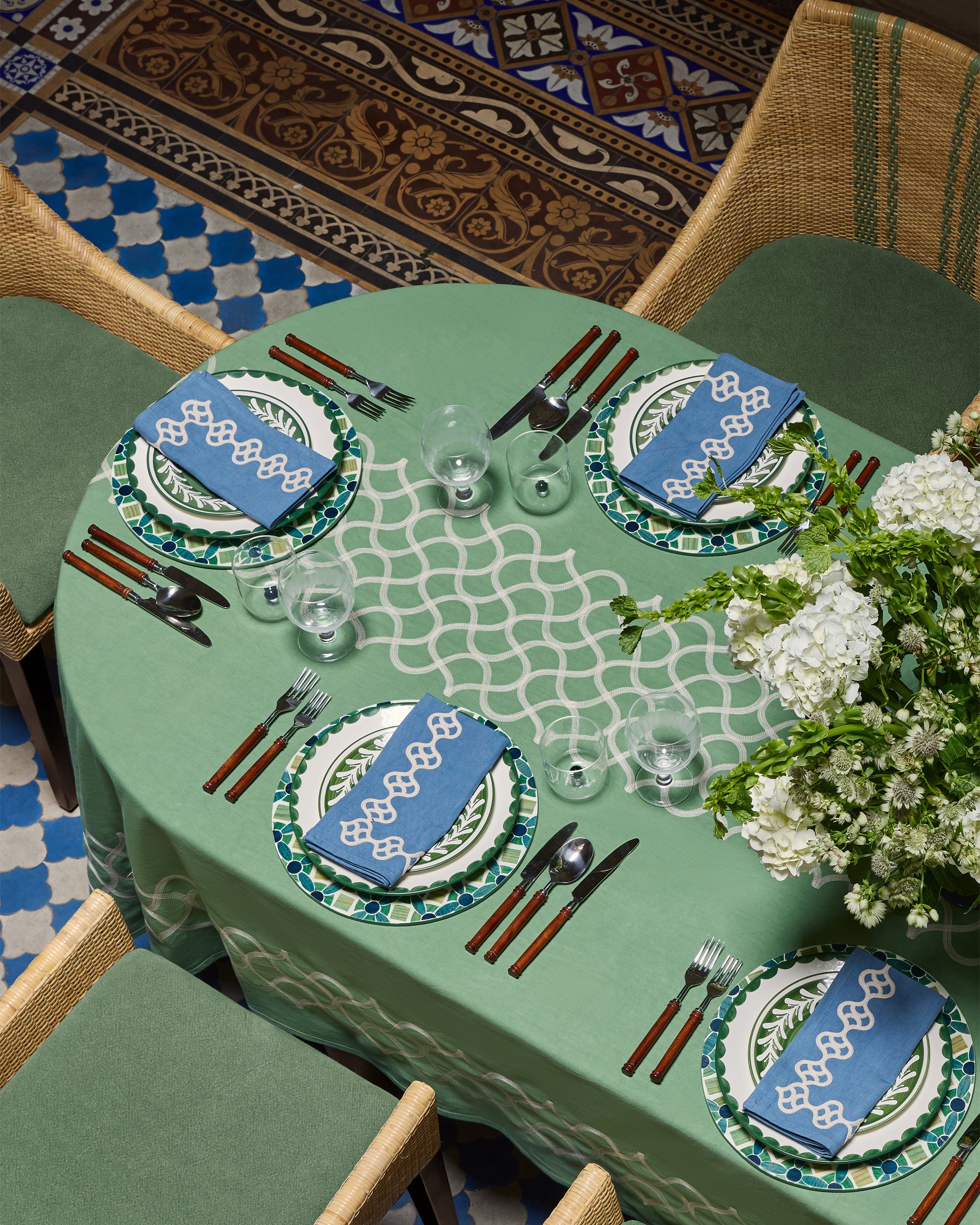 Dining table set with green tablecloth, blue plates, and white flowers.