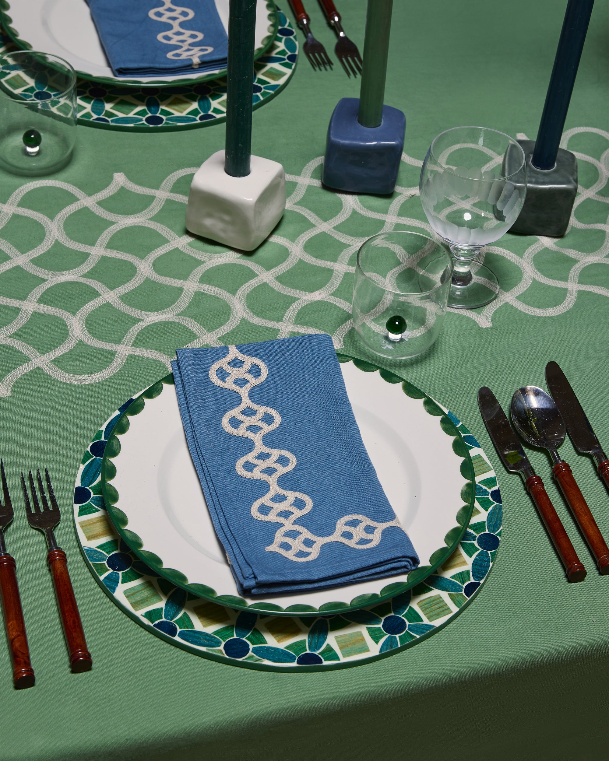 Dining table setting with decorative plates, napkins, and cutlery on a green tablecloth.