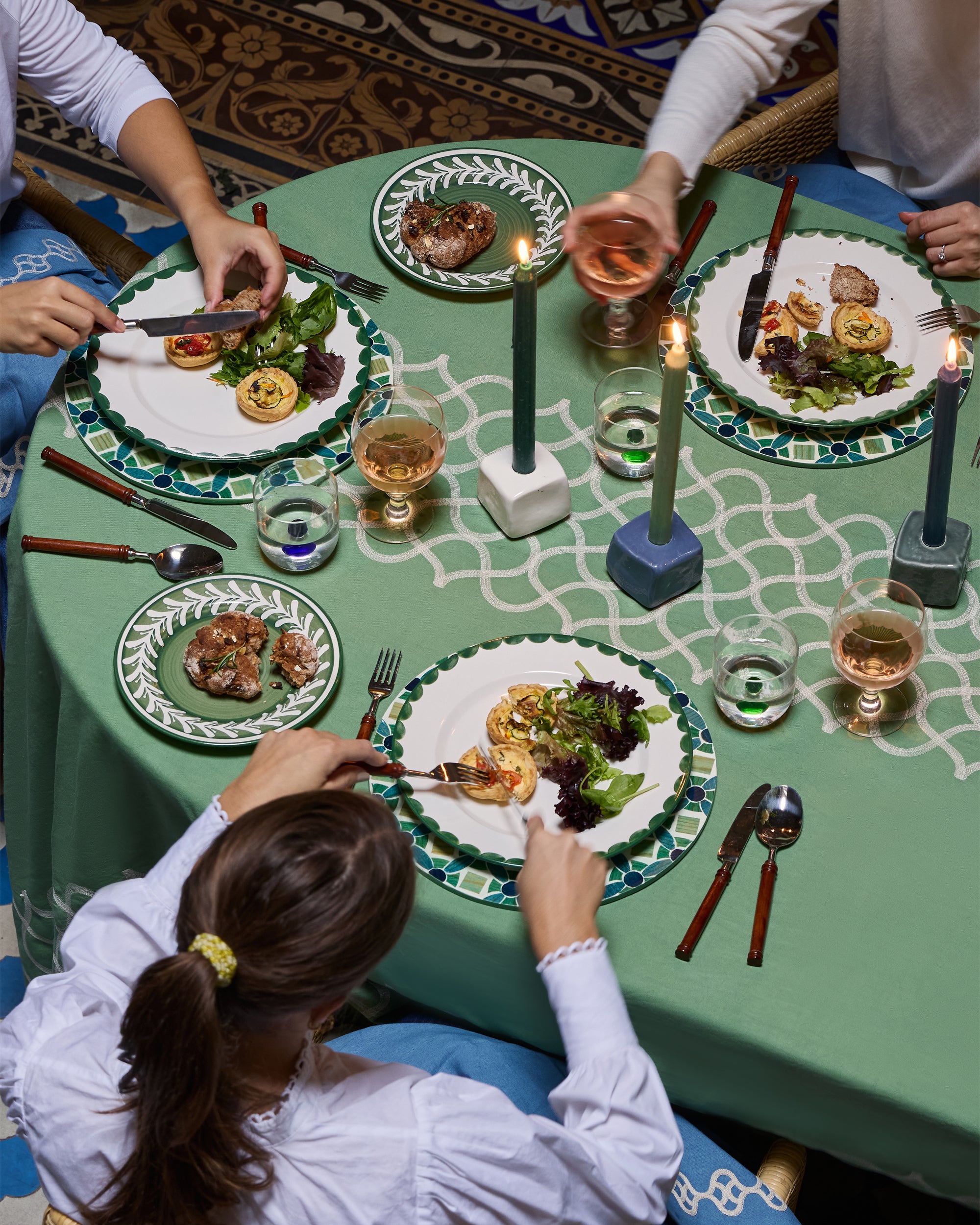 People enjoying a meal together at a table with green tablecloth and decorative plates.