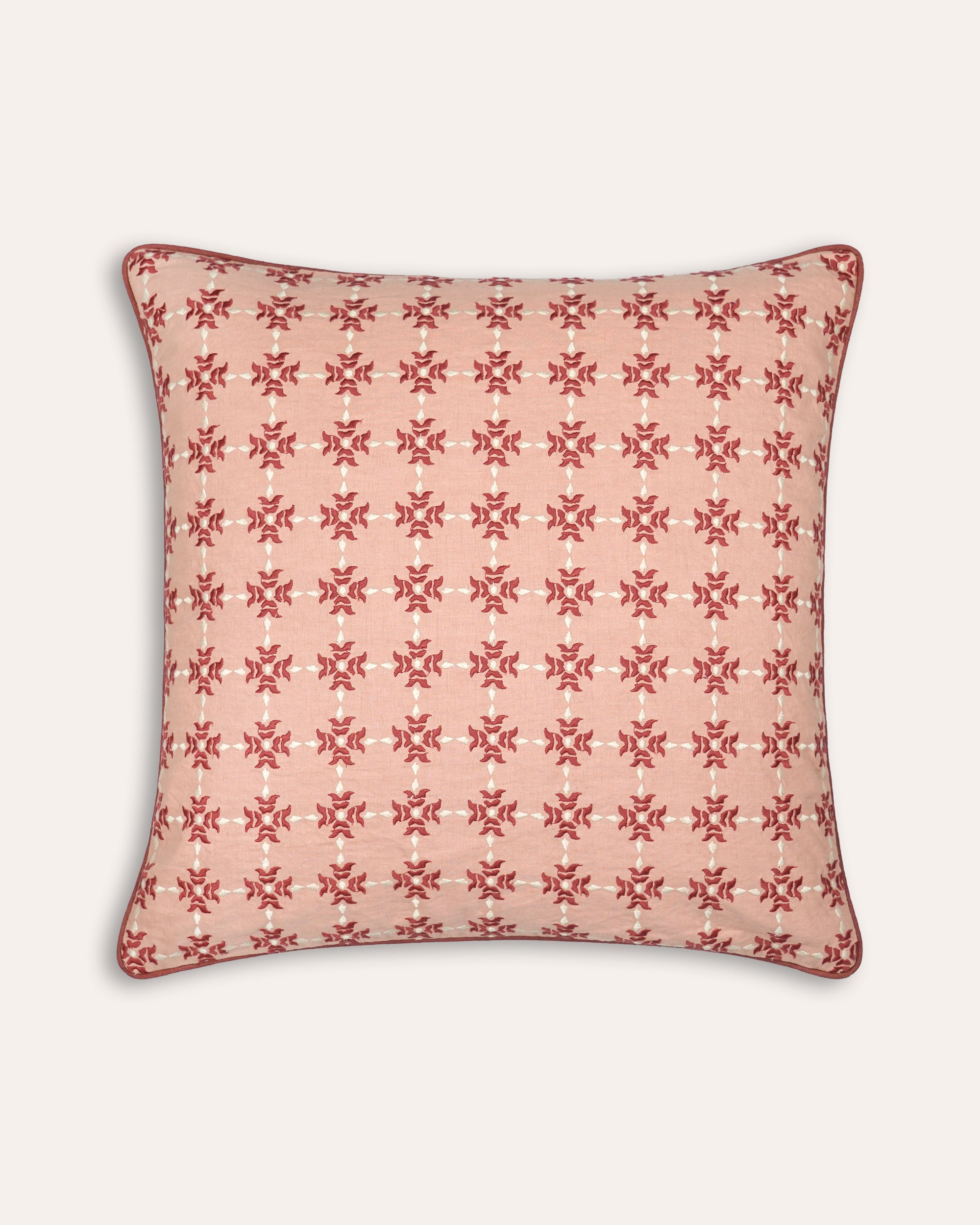 Decorative square cushion with a red geometric pattern on a light pink background