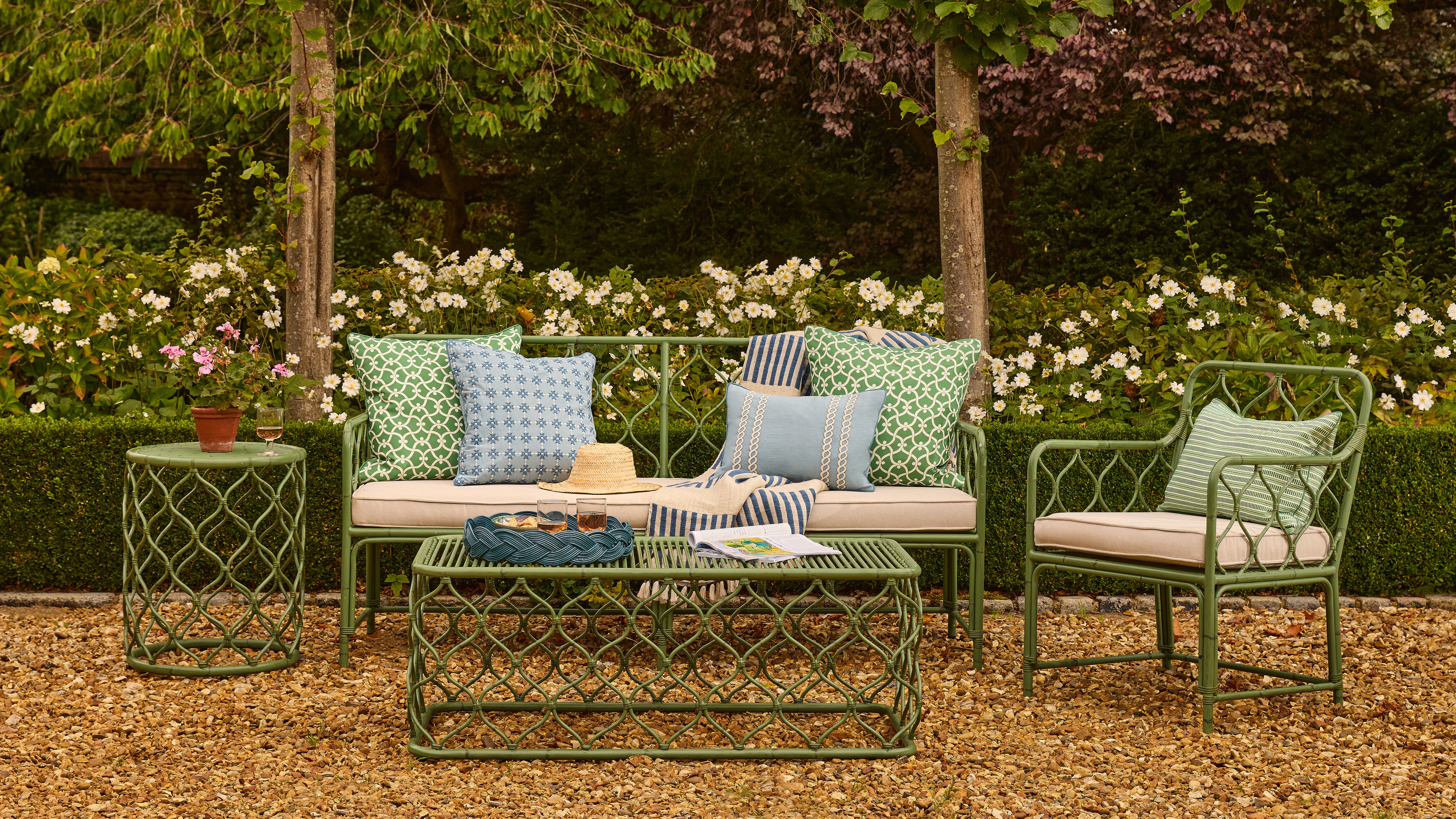 Outdoor patio set with green metal furniture, cushions, and a small table in a garden setting.