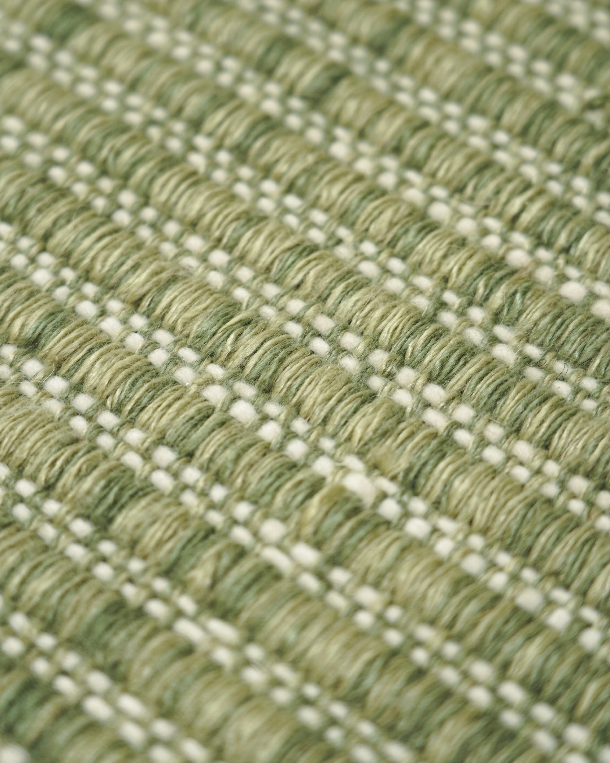 Close-up of a woven rug with a textured pattern of olive green and cream threads.