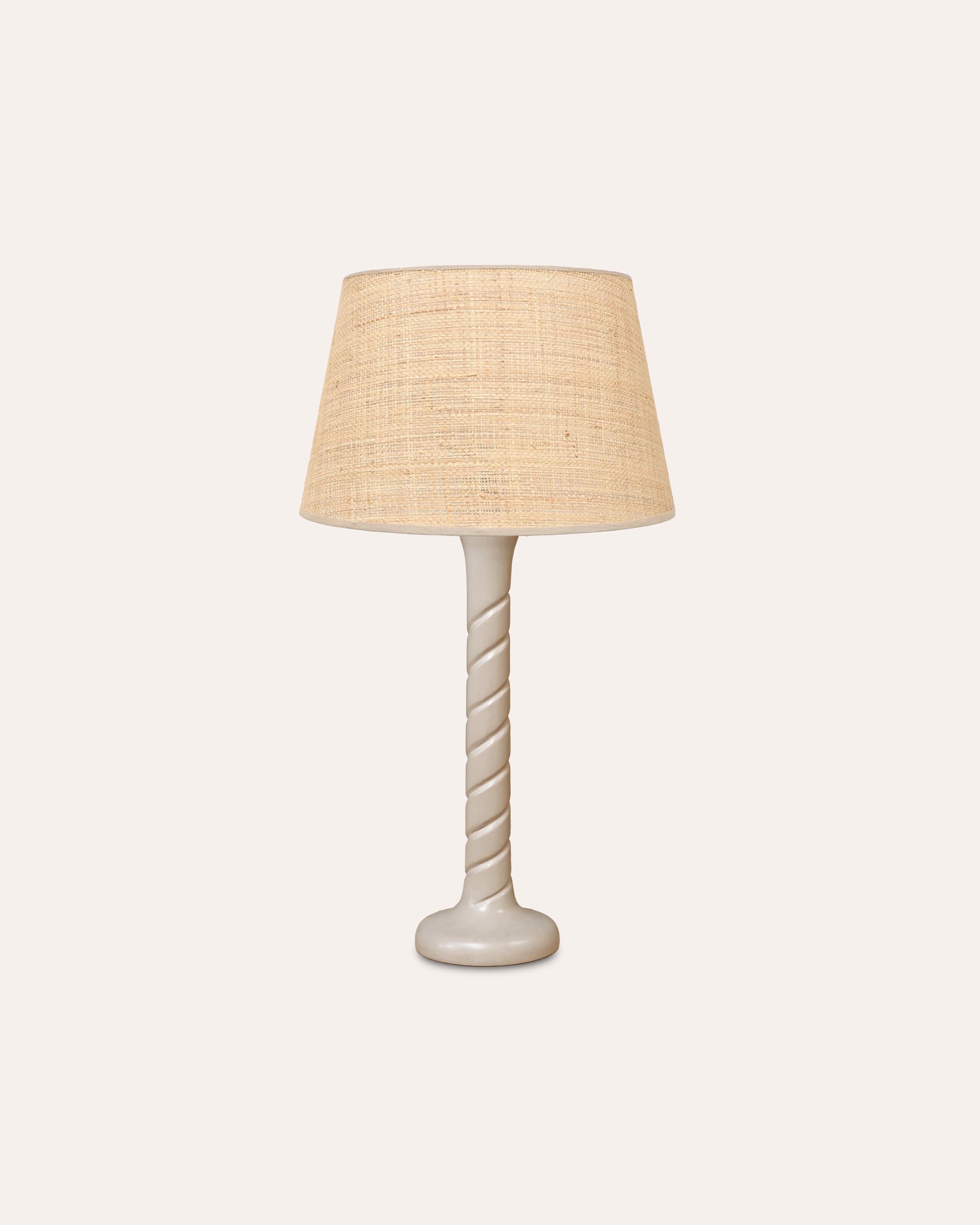 A small twisted wooden table lamp with a taupe color, hand-carved and topped with a beige lampshade.