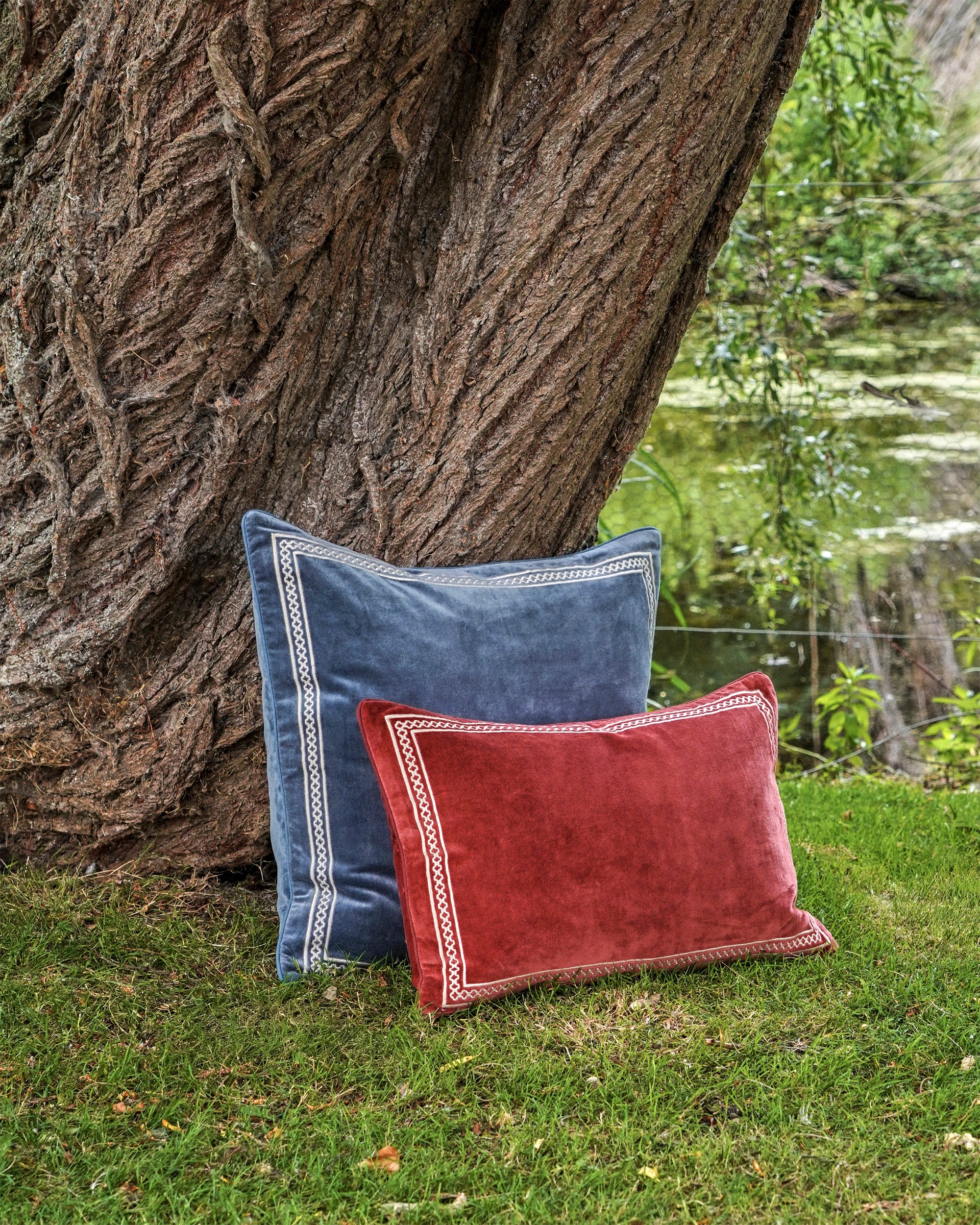 Two pillows, one blue and one red, leaning against a tree trunk with a natural background.