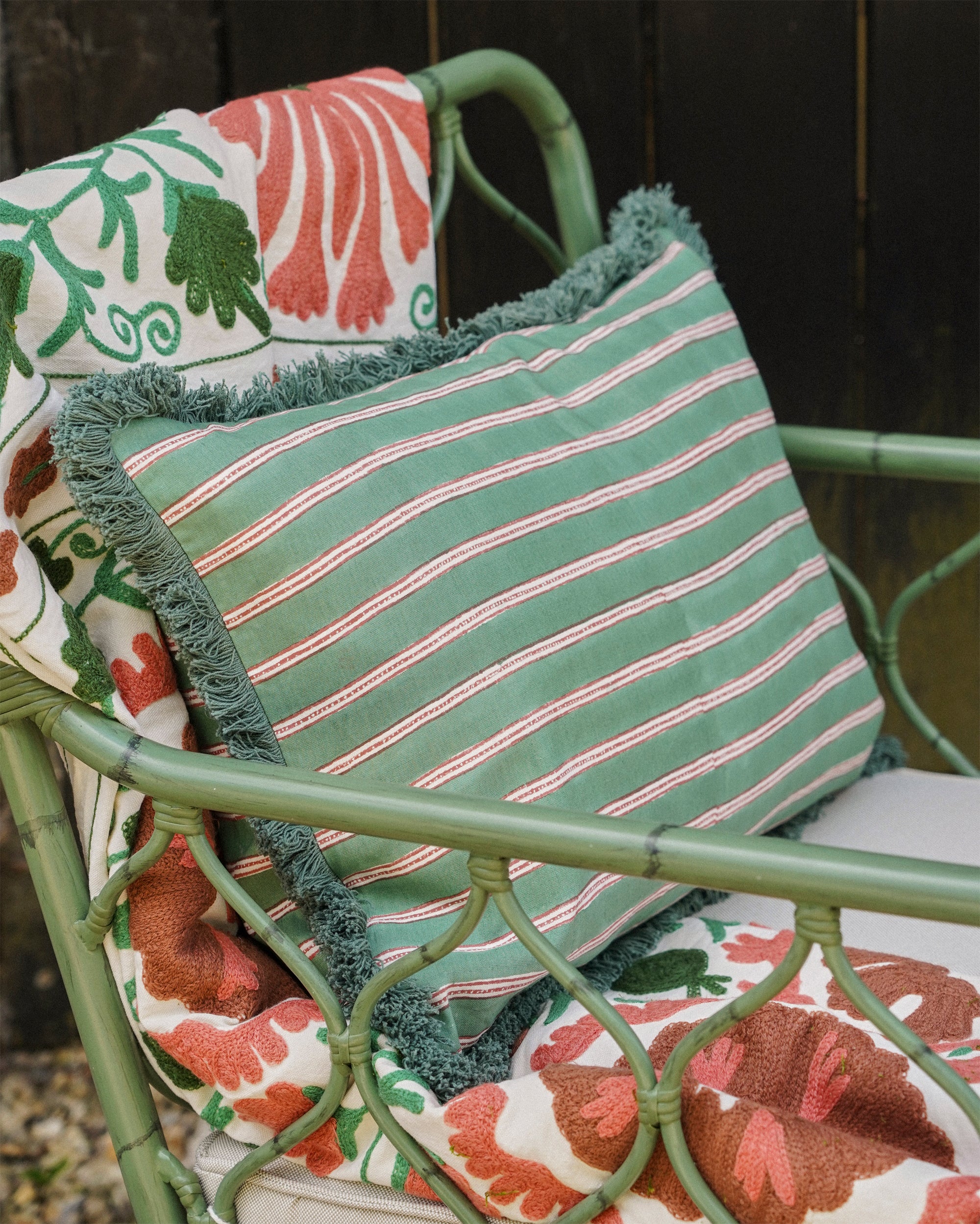Green wicker chair with a floral cushion and striped pillow.