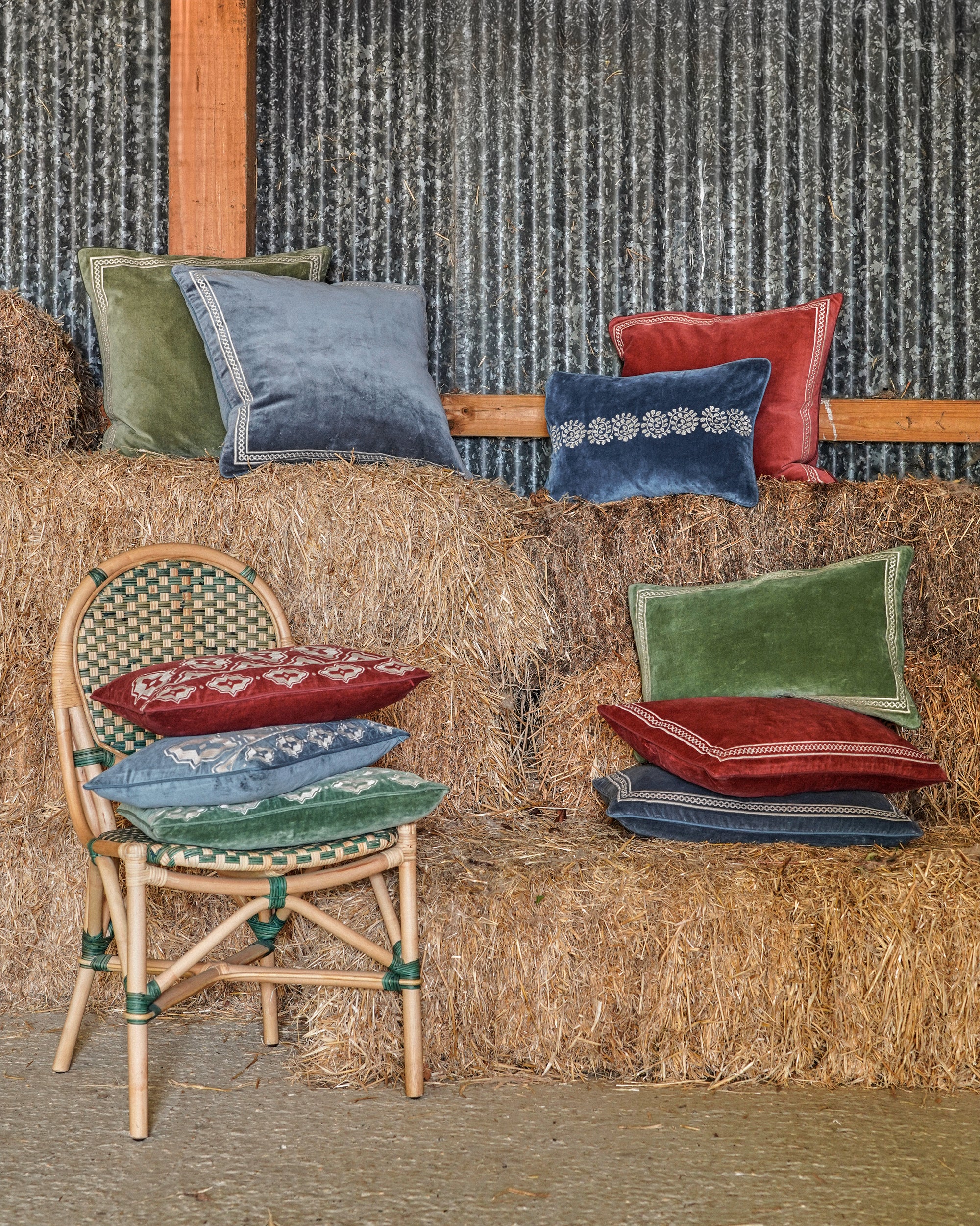Colourful pillows on hay bales with a chair nearby against a textured wall.