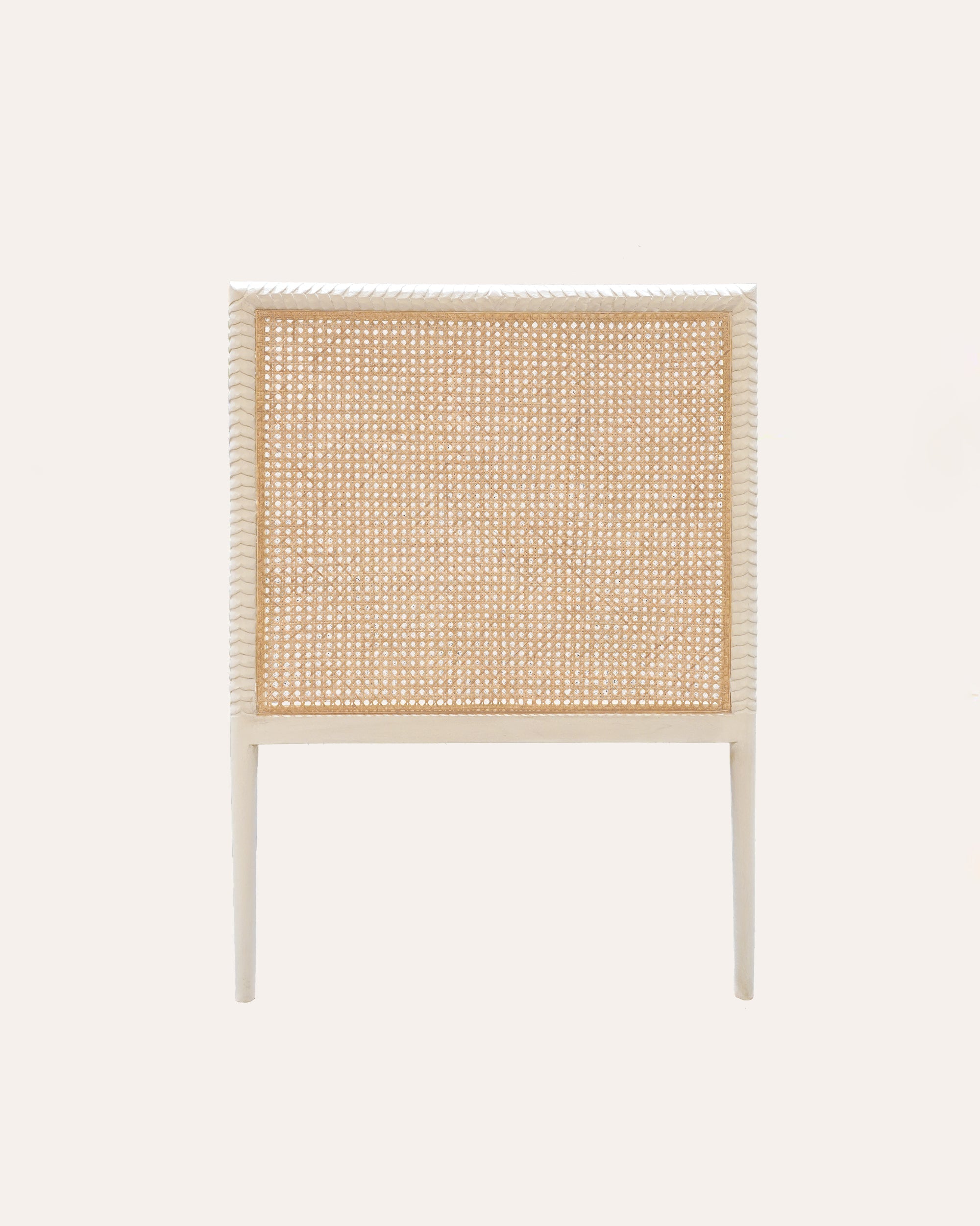 A single wooden headboard with a carved leaf motif and a natural cane finish in a taupe color.