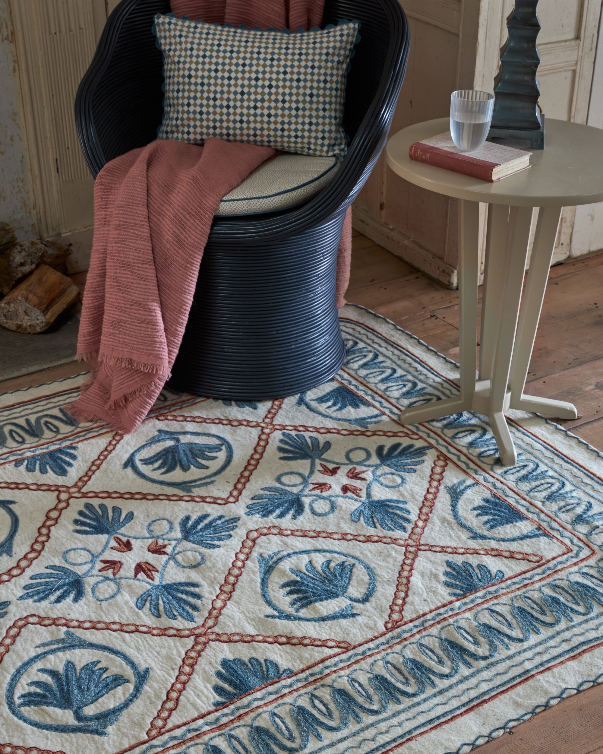 Decorative blue and red Namda rug with intricate patterns in a room setting with a chair and table.
