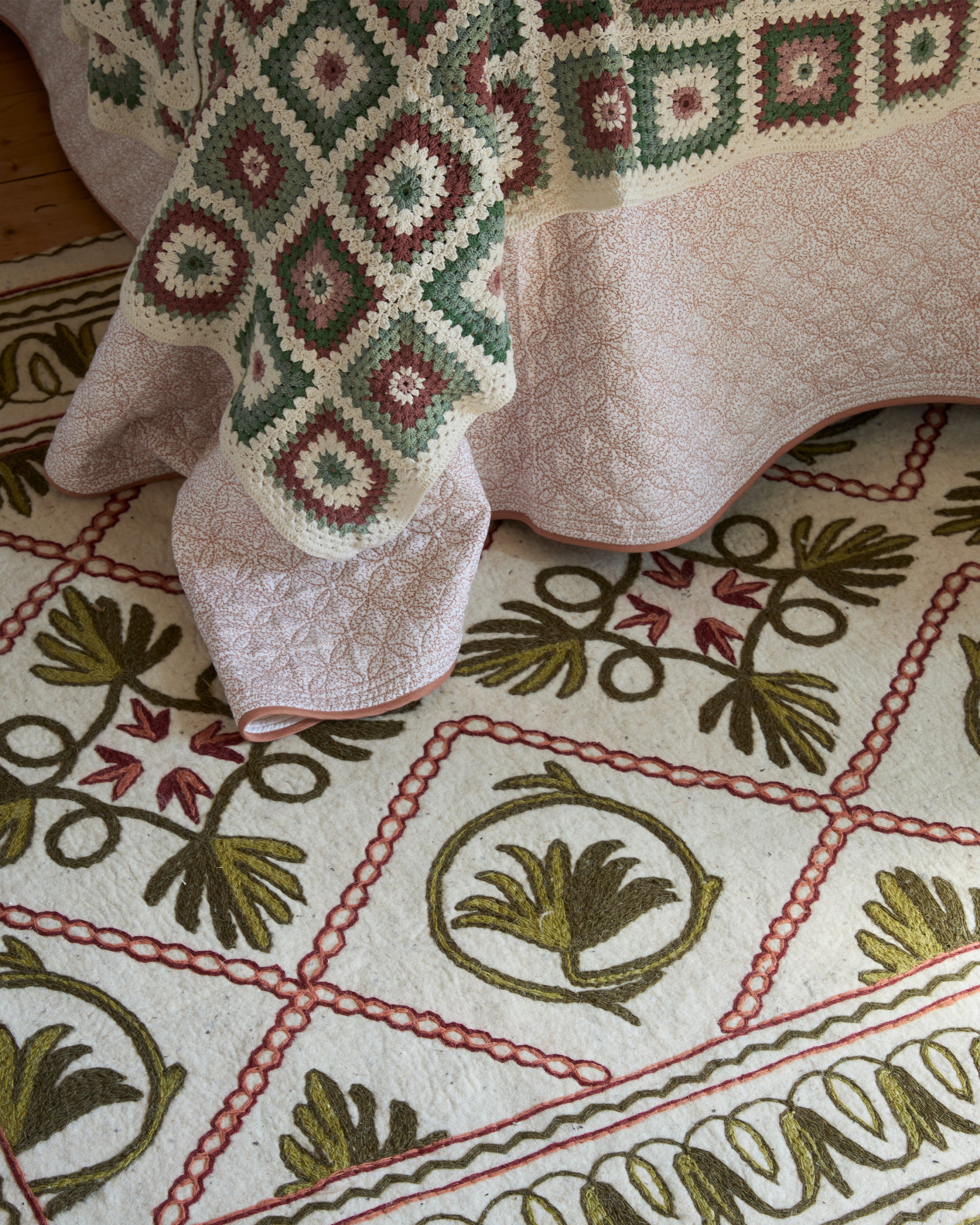 Close-up of a green and red Namda rug with embroidered designs on a wooden surface.
