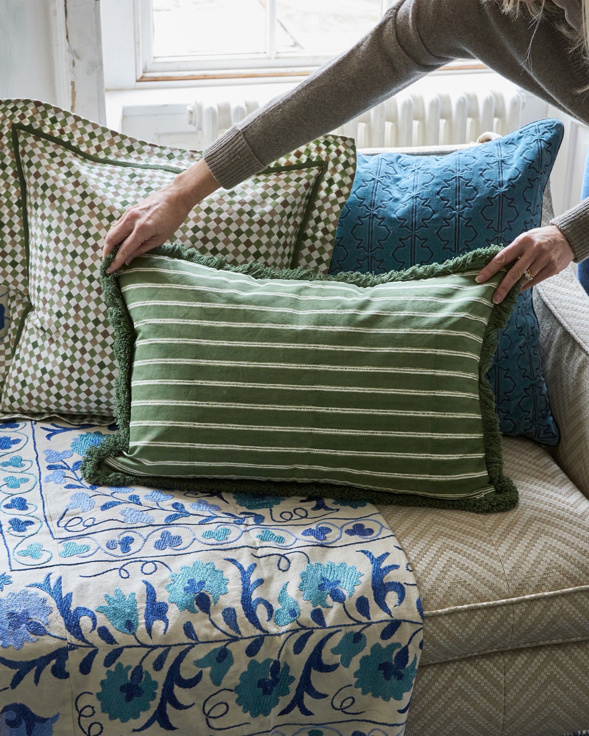 Person arranging the green edo striped rectangular cushion on a sofa with floral blanket