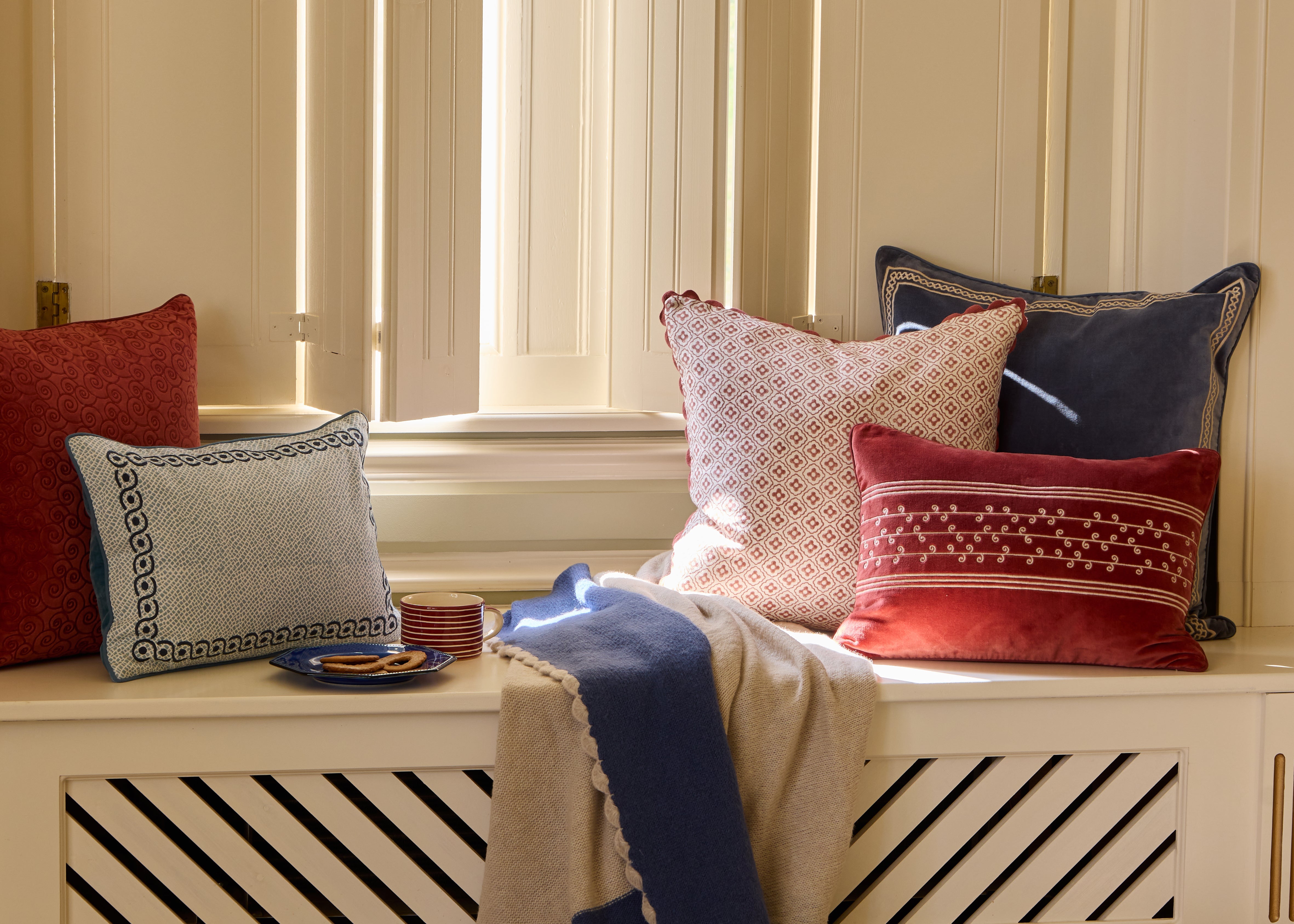 Birdie Fortescue Soft Furnishings - A range of blue, pink and red cushions on a window seat