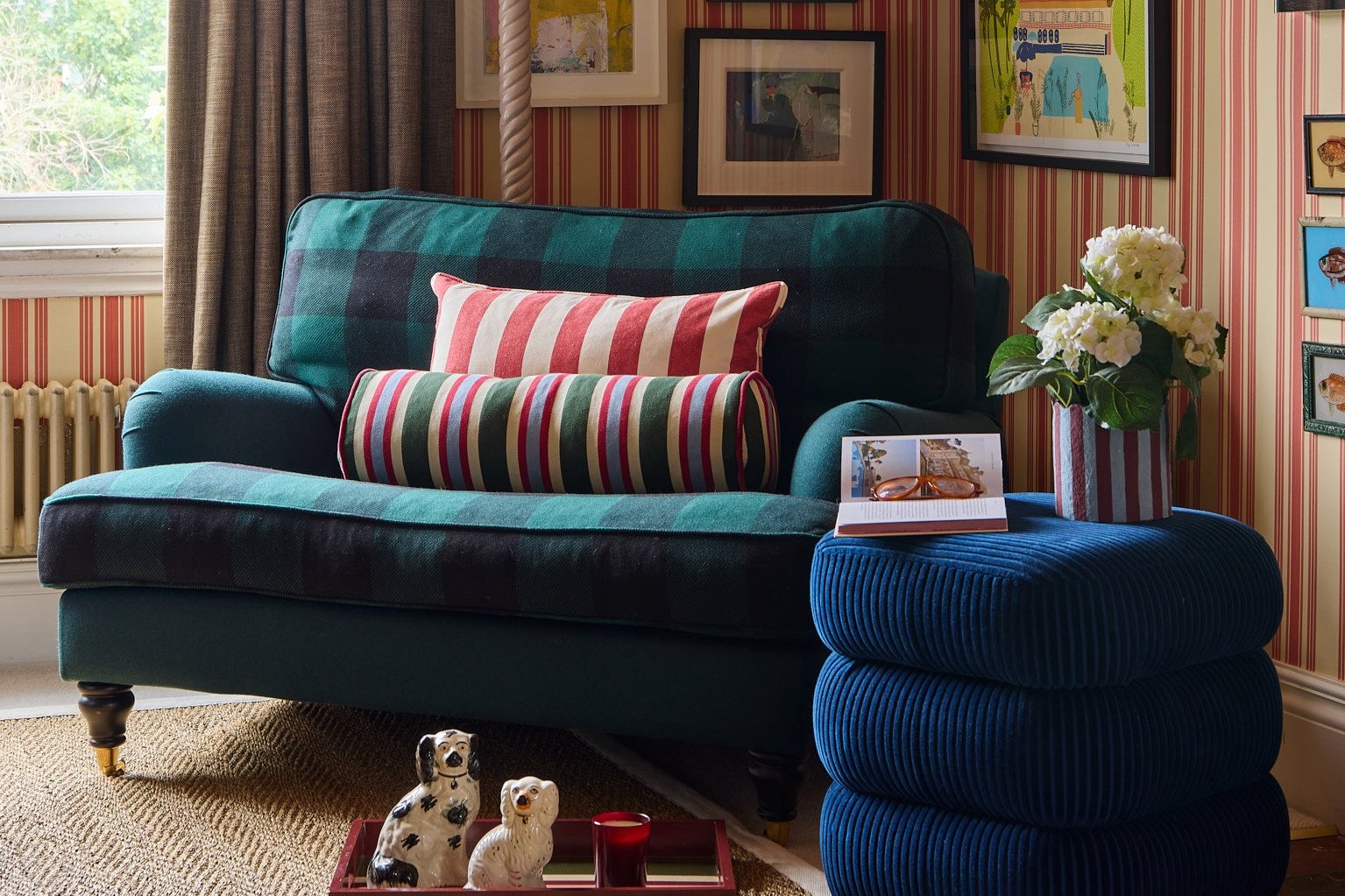 Bolster striped cushion on a green checked armchair, with a blue classic stool next to the chair