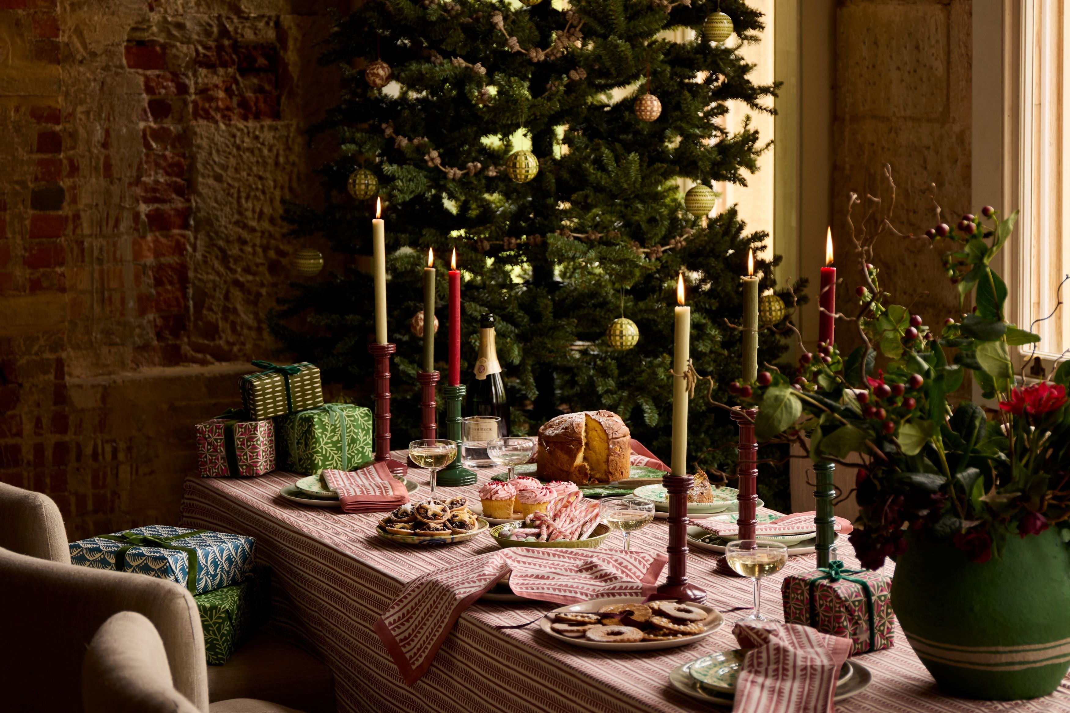 A christmas dining table with food, candles and a tree in the backgroundd