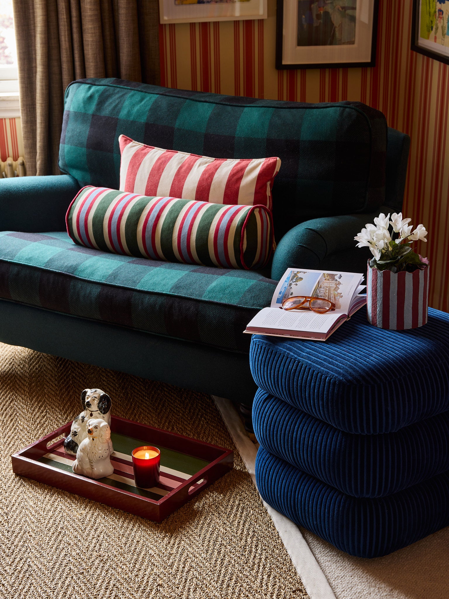 The stripes galore bolster cushion sit on an armchair next to the classic stool in blue. There is a read tray on the floor with a candle on it.