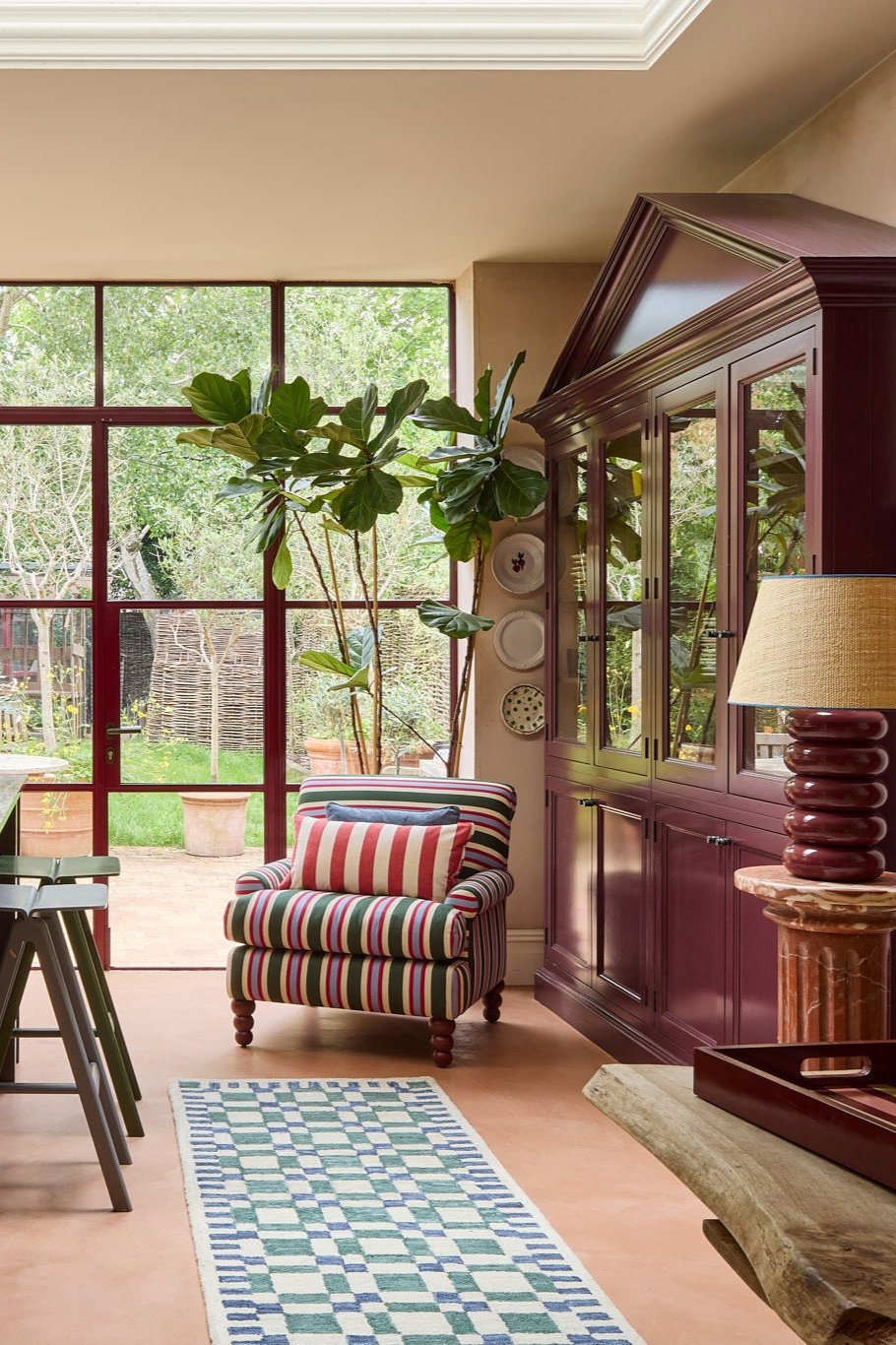 The striped heaven chair sits in front of a big window with the check mate runner in blue and green