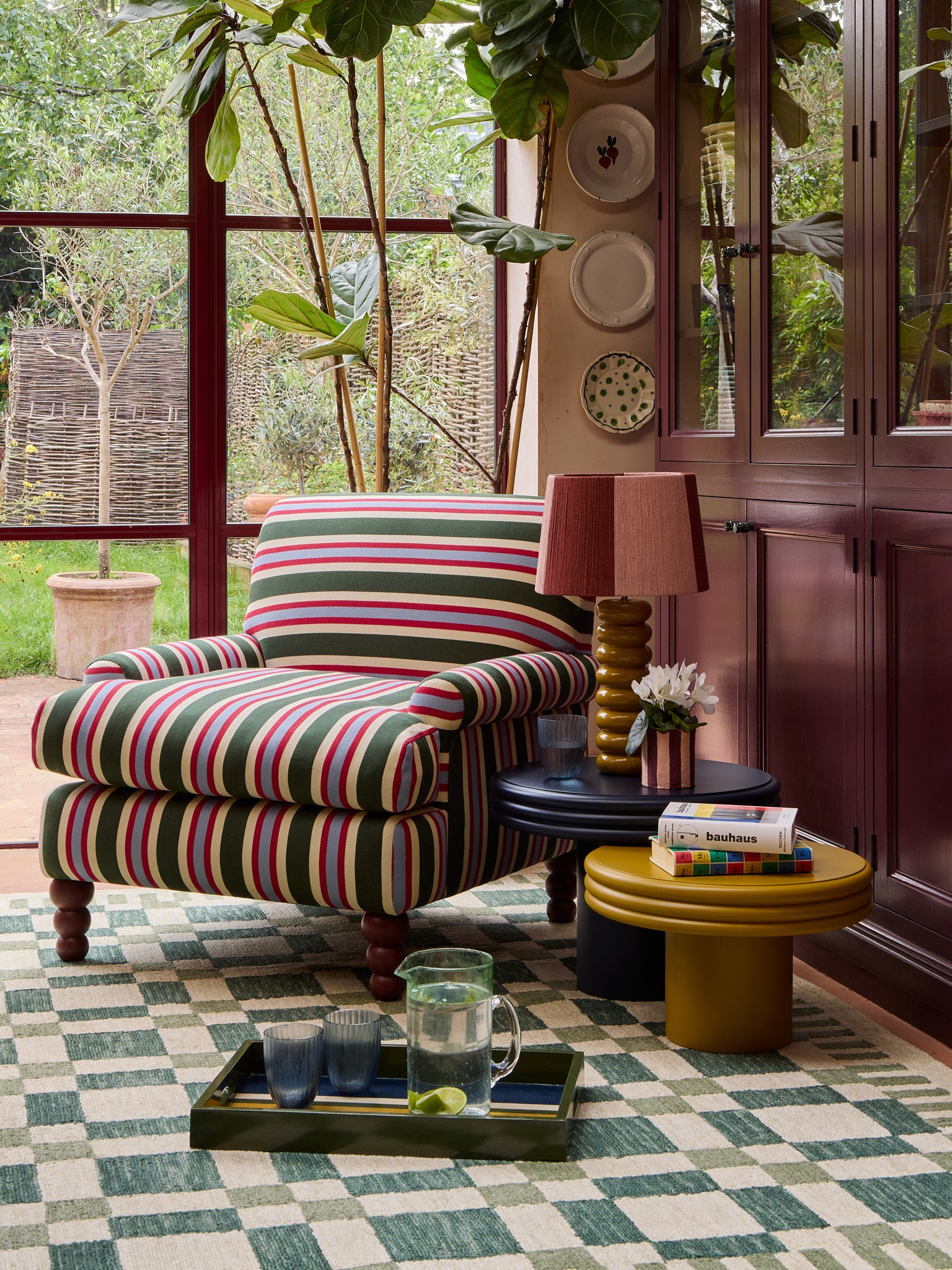 The striped heaven armchair in front of a window with the check mate  rug and a mustard yellow lamp