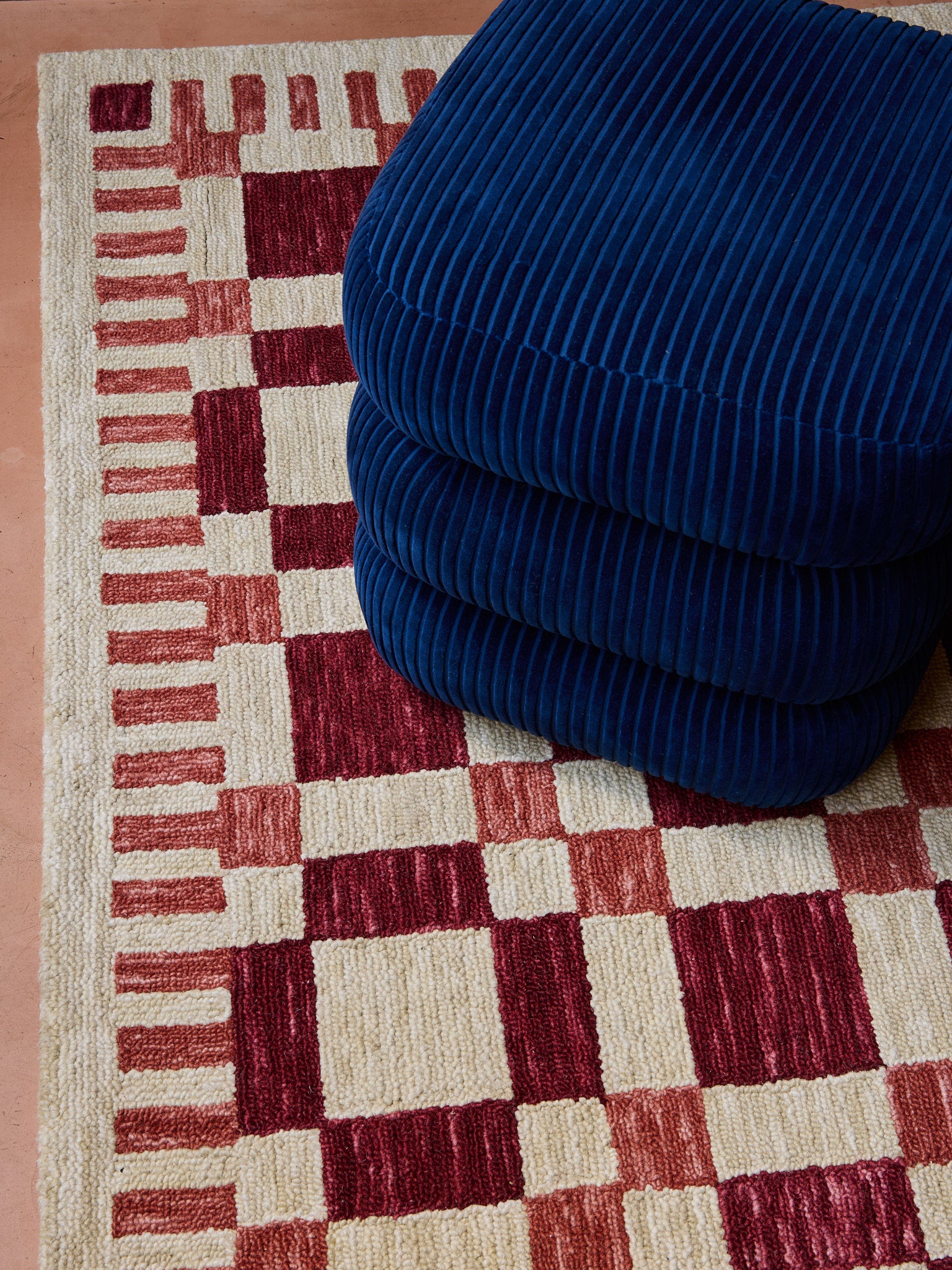 a close up shot of the classic stool in blue with the check mate rug in red