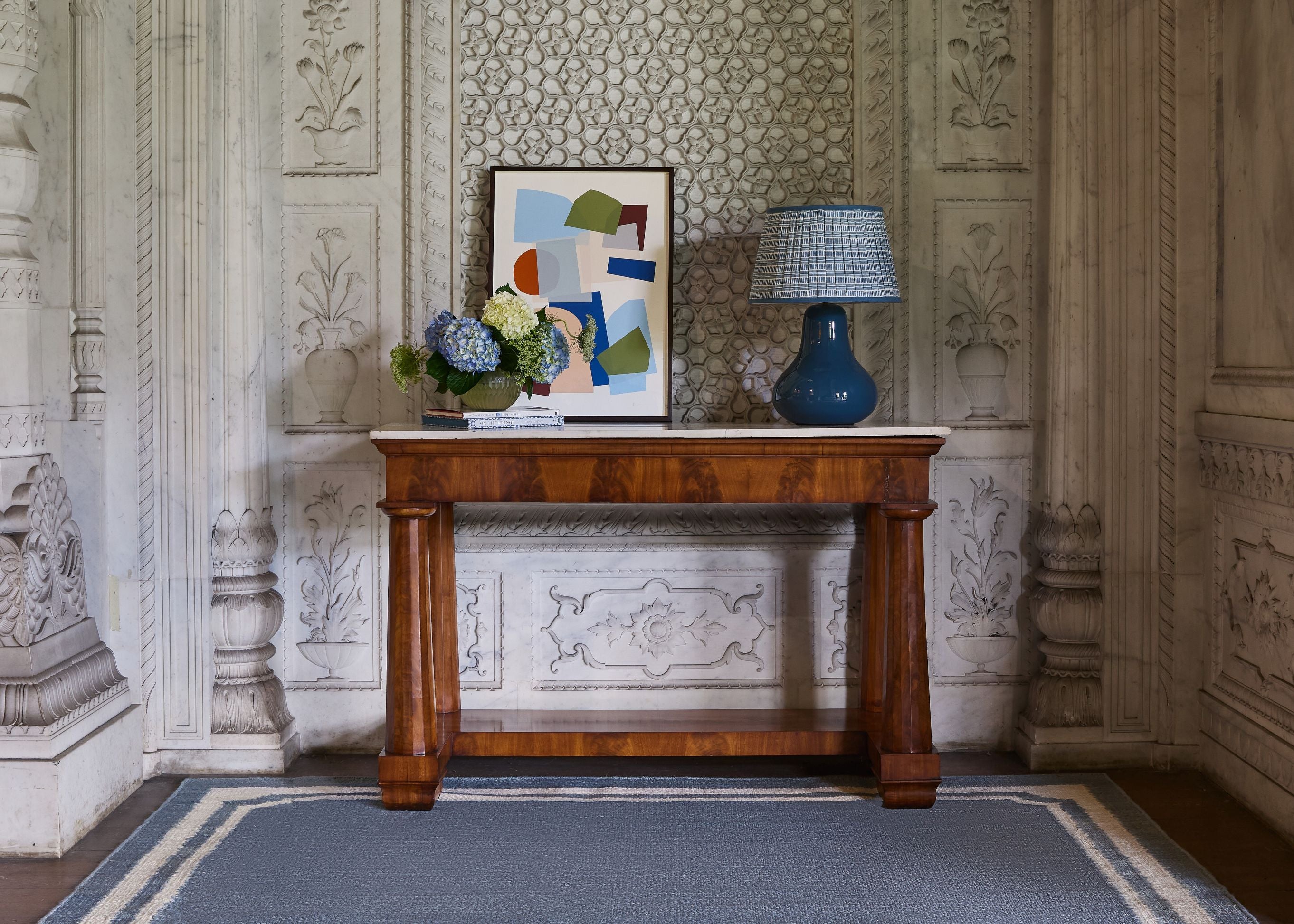 Wooden console table with decorative items against an ornate wall.