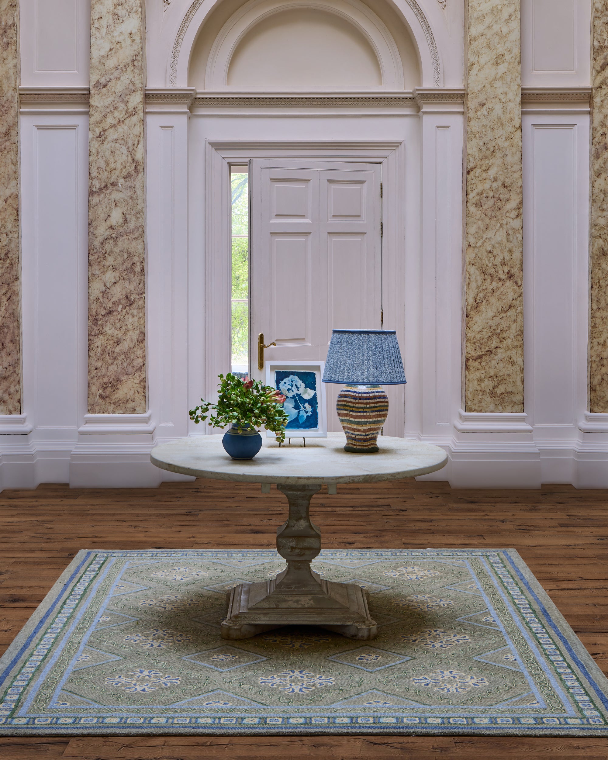 Green Varuna rug, with a white antique table on top featuring the mosaic lamp, blue remolino lampshade and small blue cotton mache vase