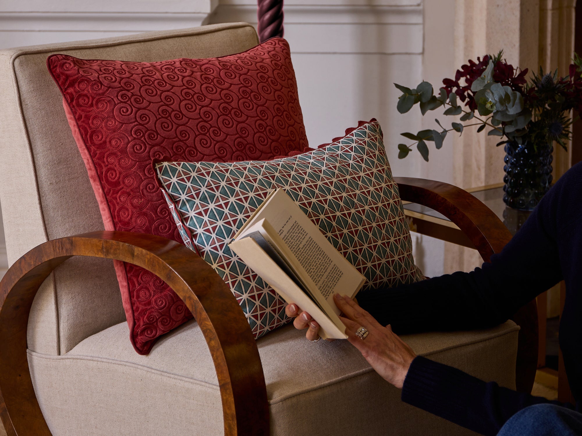 Person reading book next to armchair with blue and red cushions