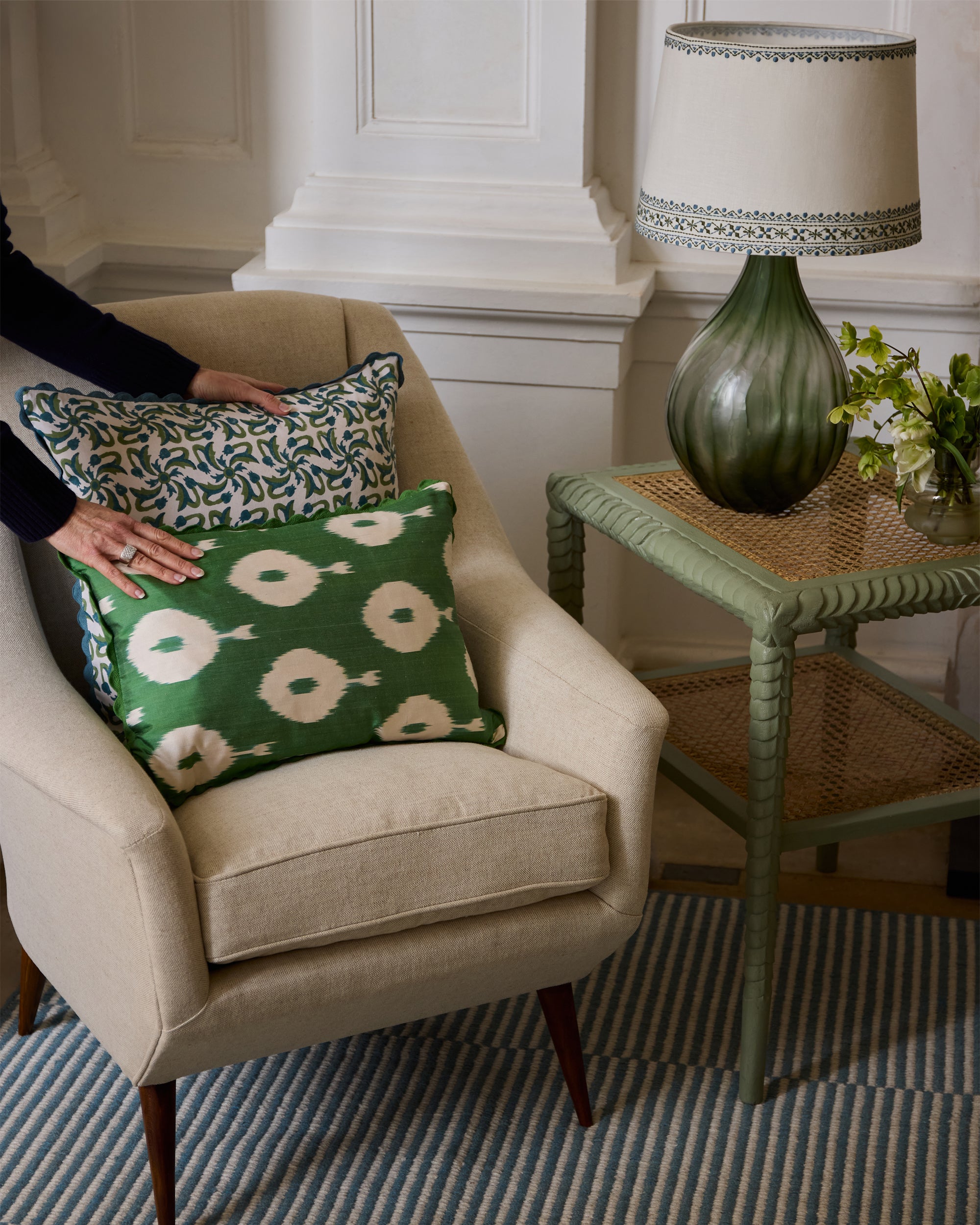 Hands placing green ikat cushion on linen armchair