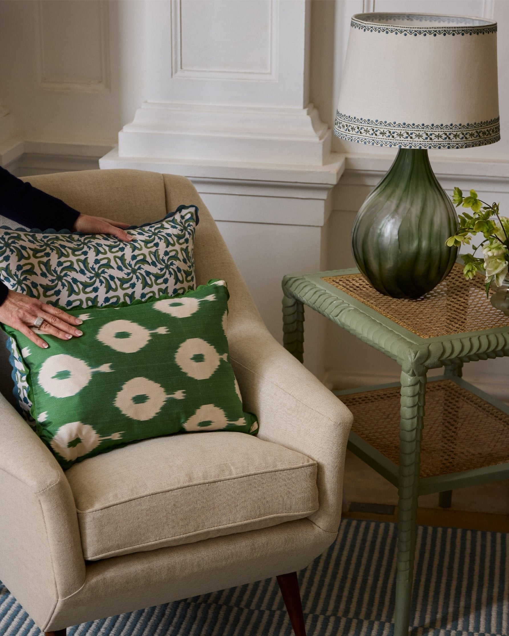 Image of hands arranging green ikat cushion on a linen chair