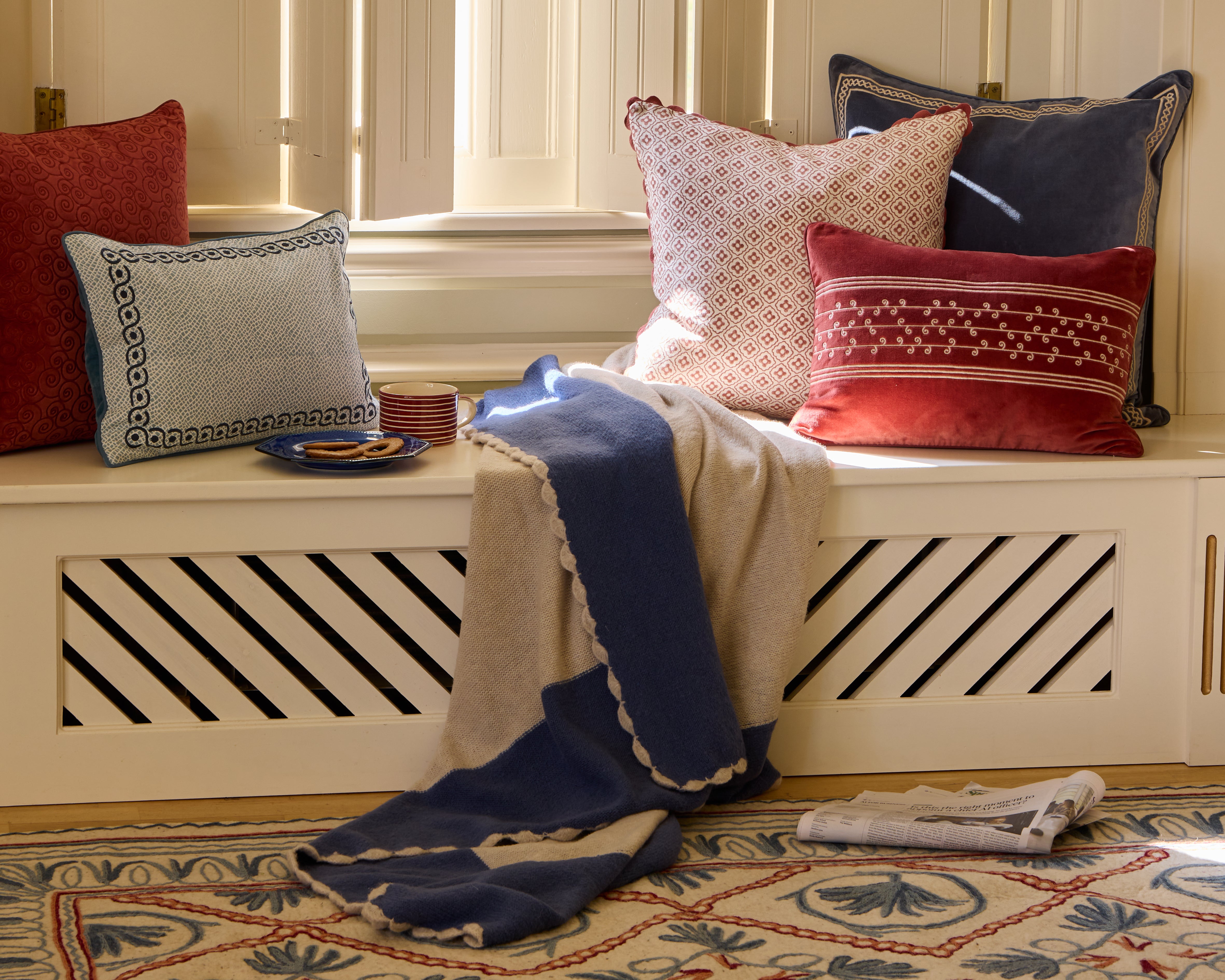 Relaxing window seat lifestyle image featuring a range of Birdie Fortescue's blue and red soft furnishings