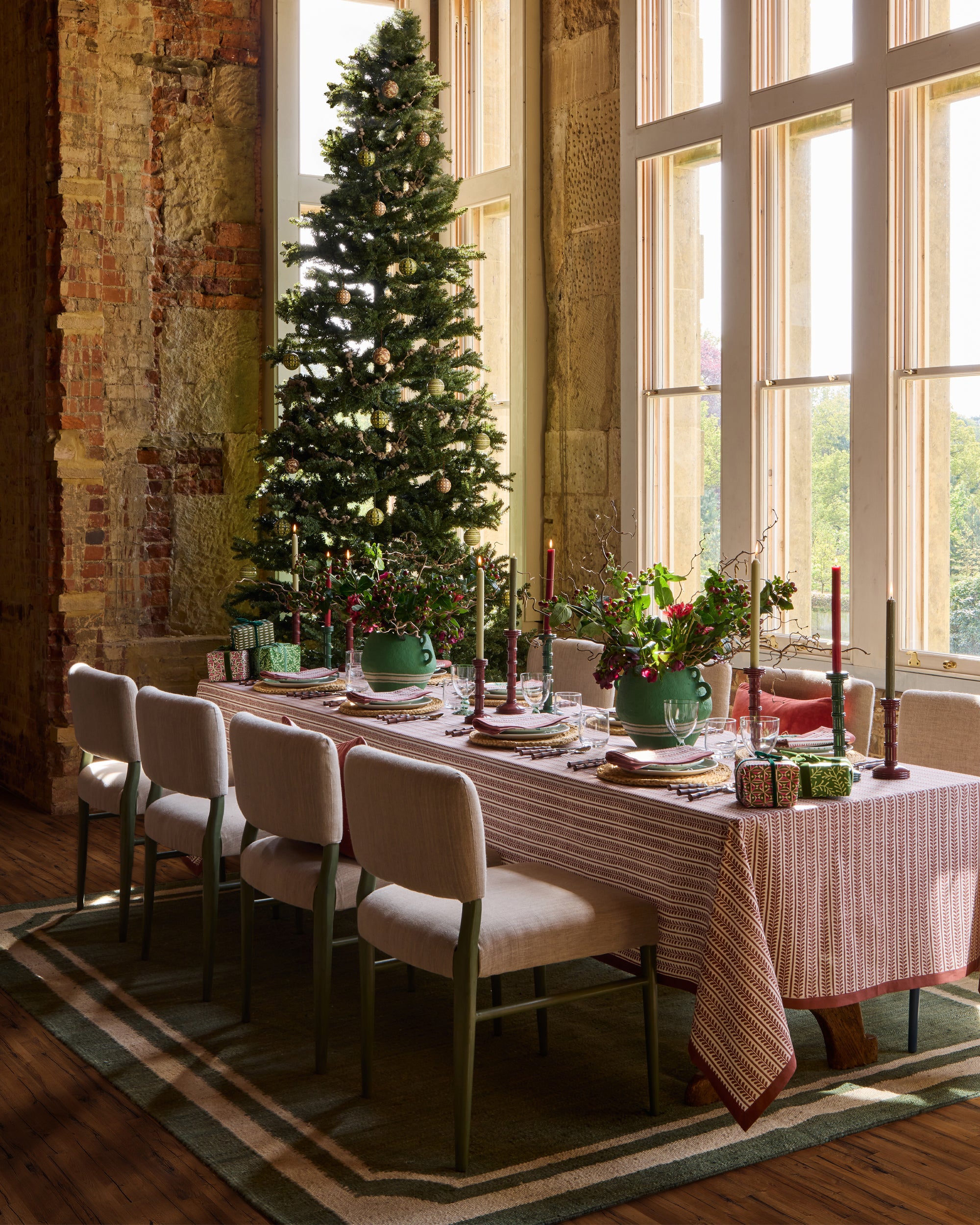 Festive dining tablescape featuring, red bel table linens, large green cotton mache vases and red and green column candlesticks